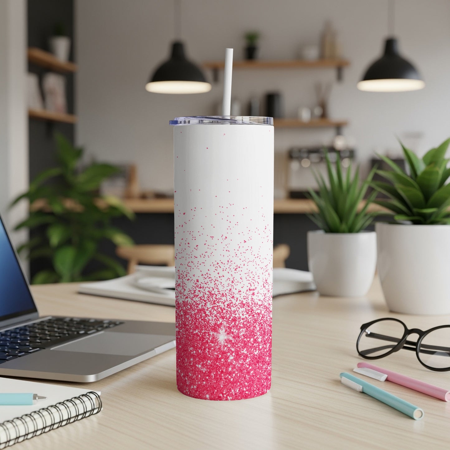 White tumbler with pink glitter ombre on wooden desk with laptop and pens.