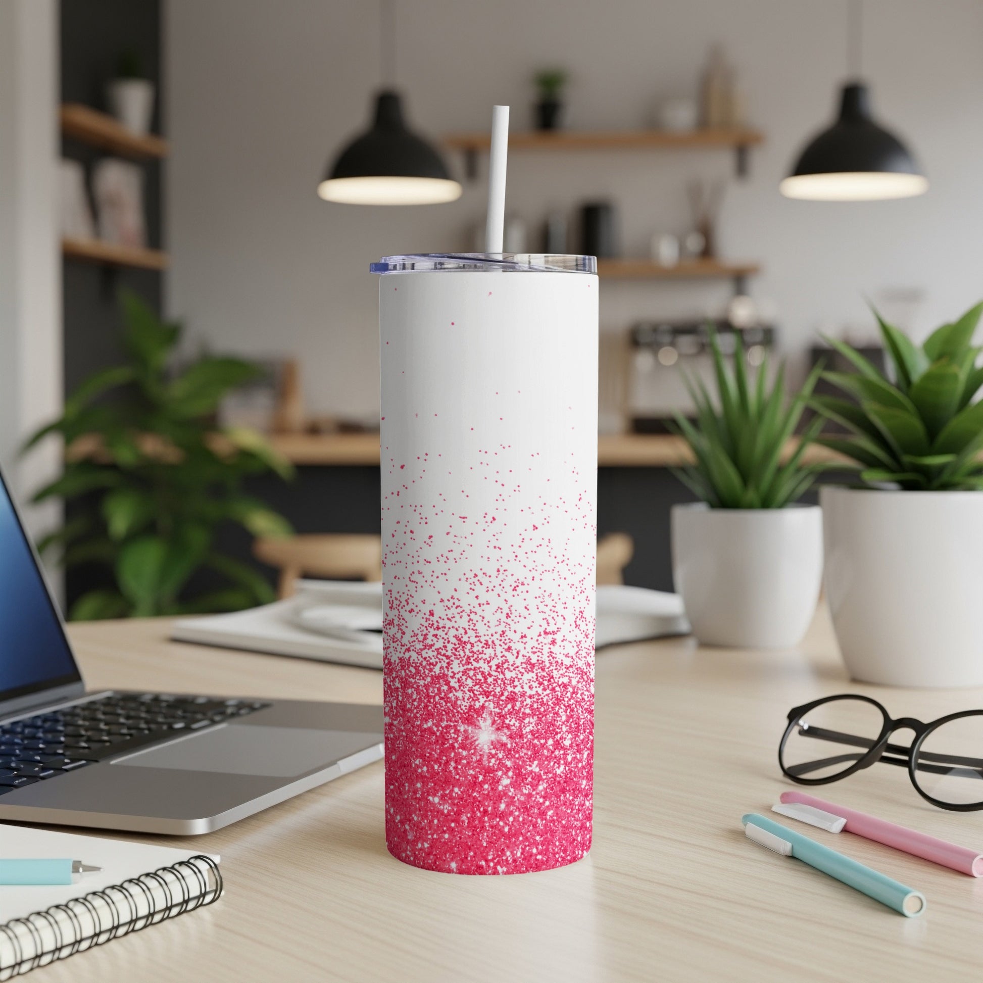 White tumbler with pink glitter ombre on wooden desk with laptop and pens.