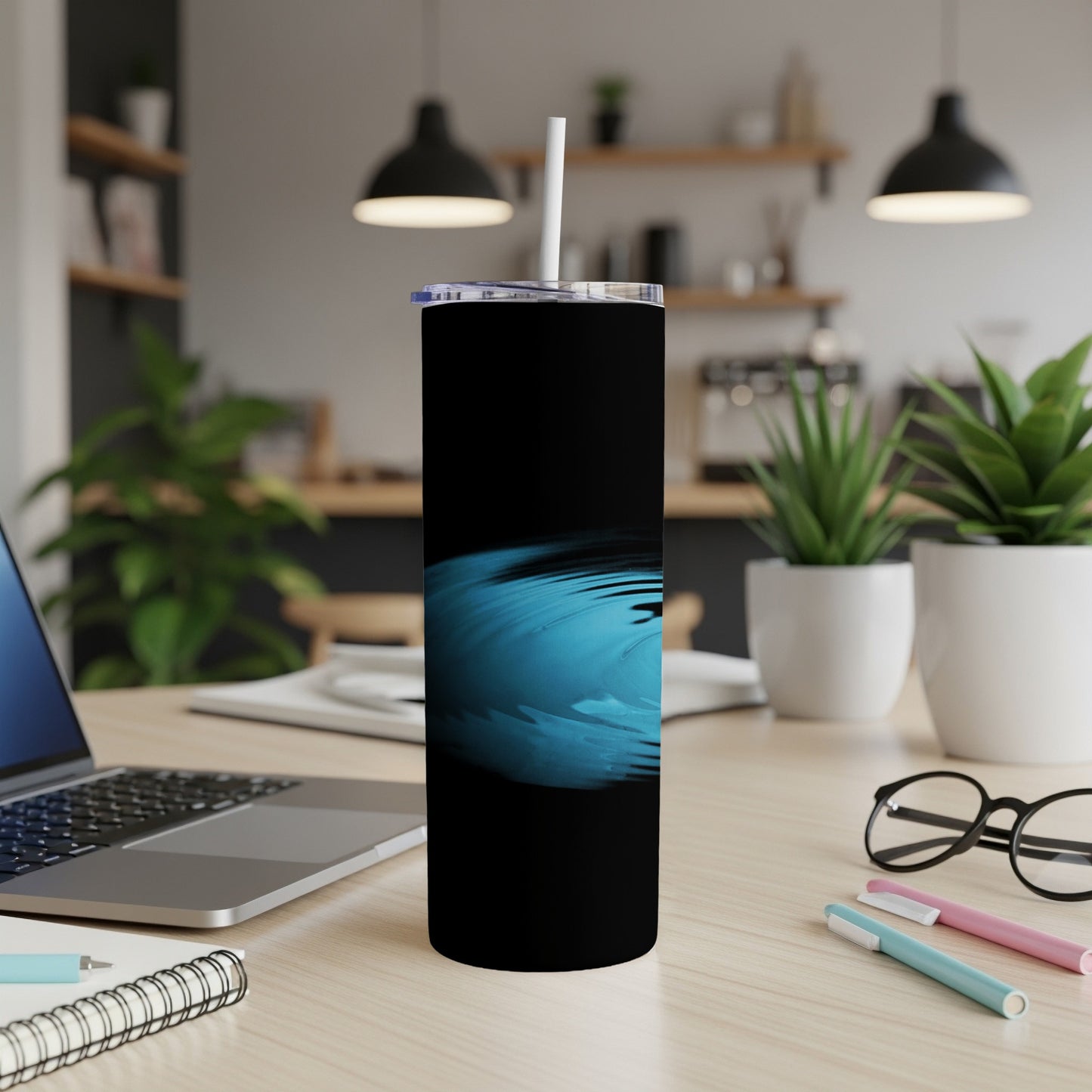 Black tumbler with blue wave graphic, straw, and office desk background.
