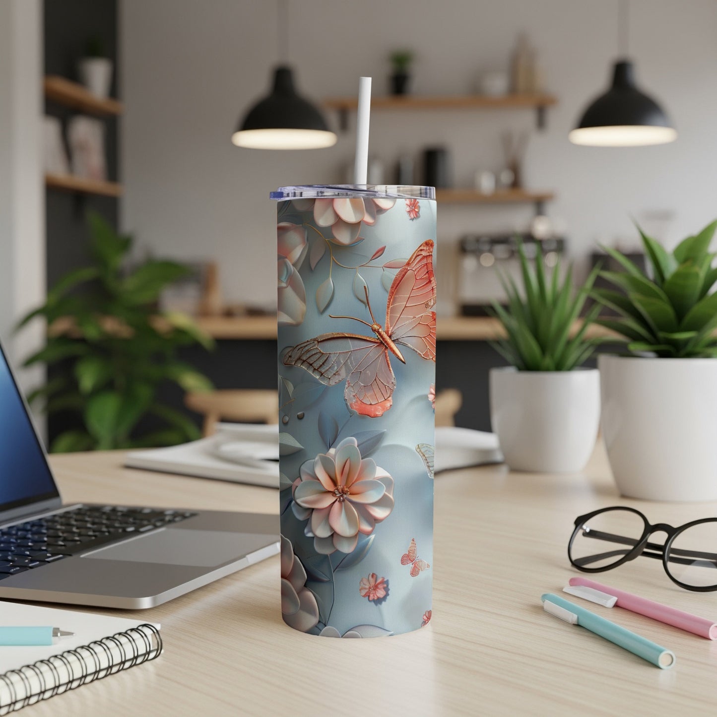 Blue tumbler with butterflies and flowers, straw inserted, on desk.