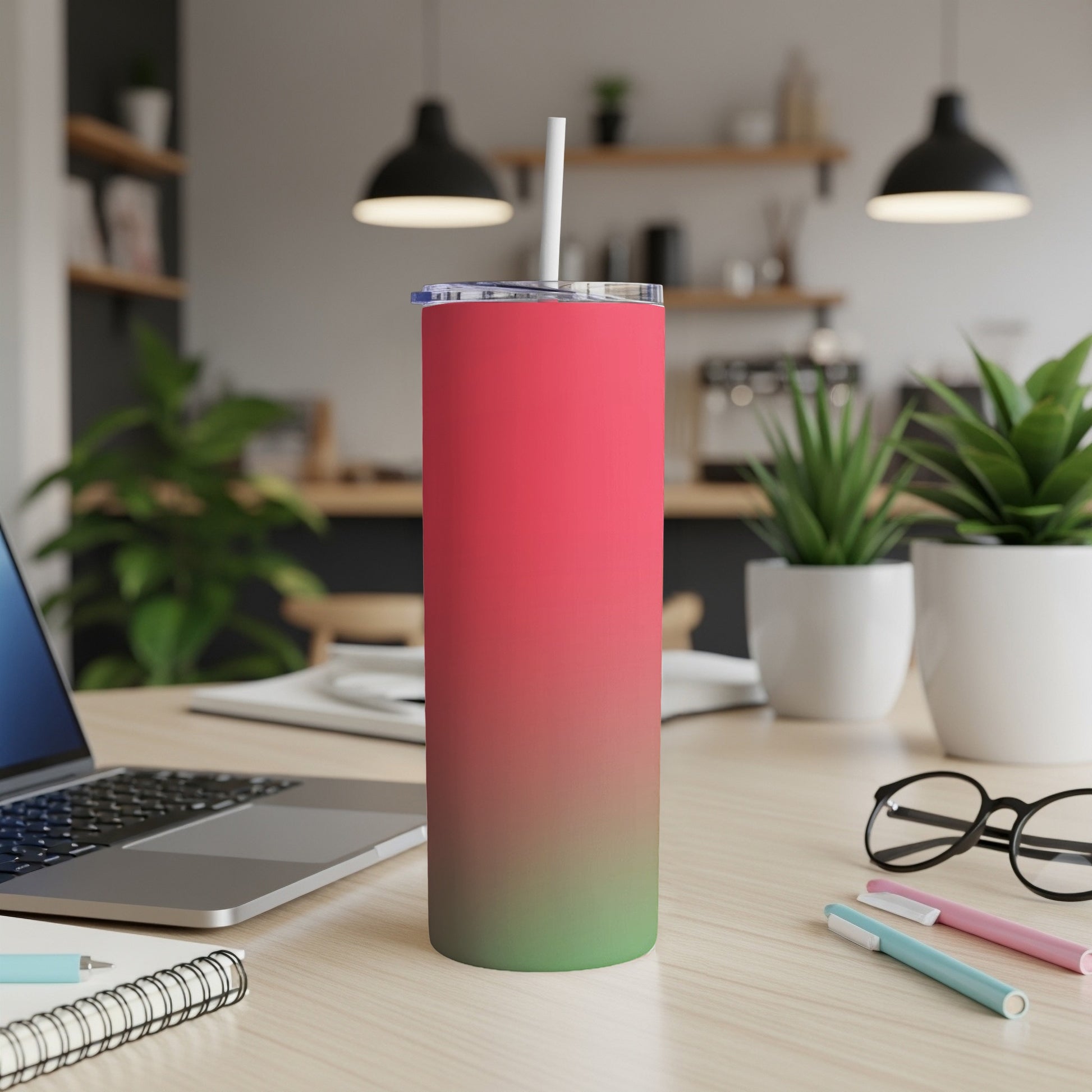 Tall pink and green gradient tumbler with straw on desk next to laptop and glasses.