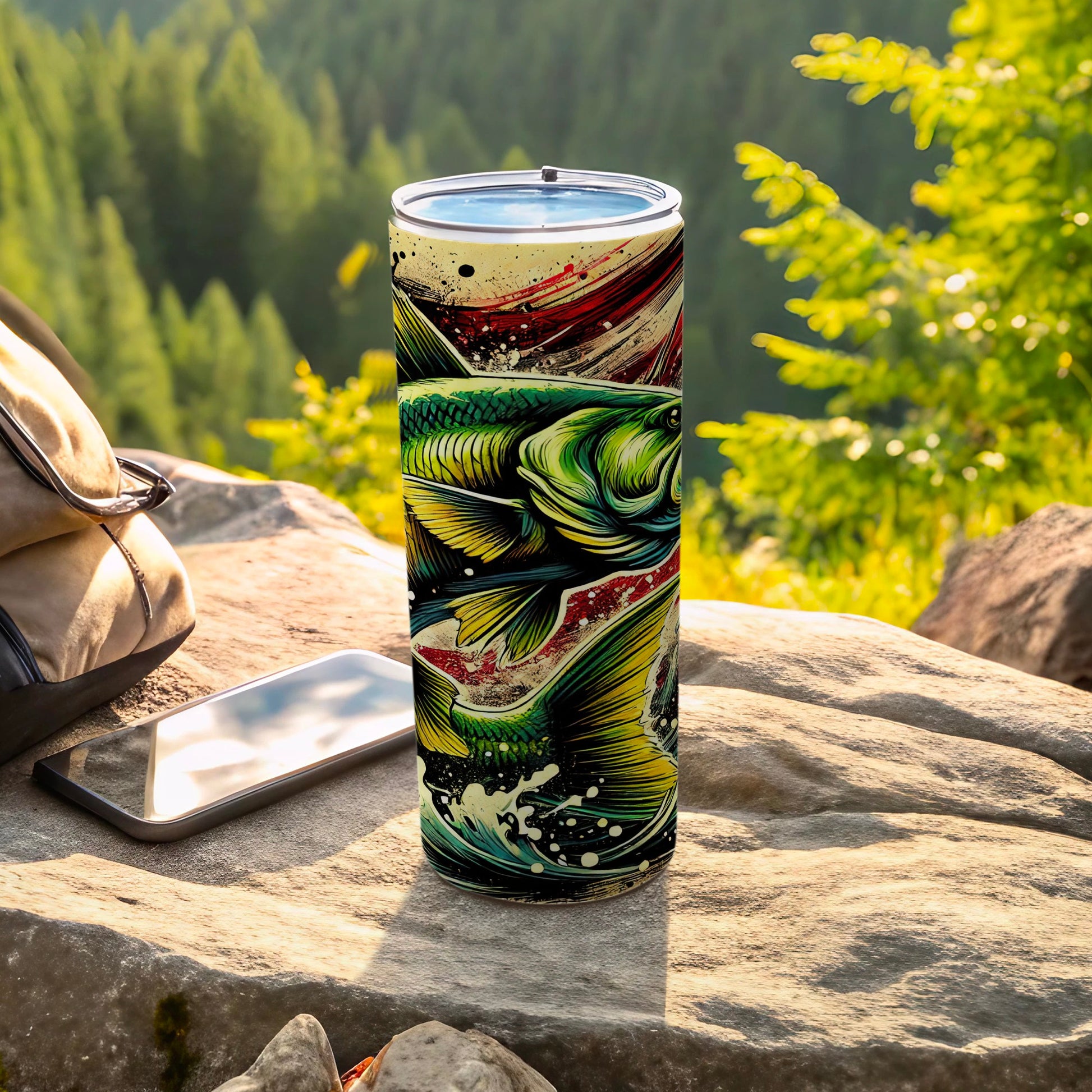 Tall tumbler with vibrant fish graphic, resting on rocks outdoors.