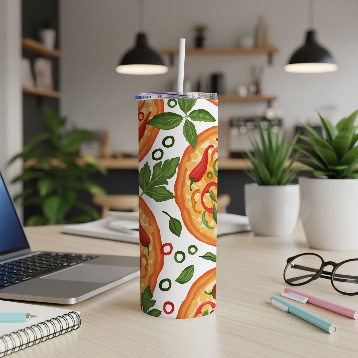 Tumbler with pizza and herb pattern, straw, laptop, glasses, and pens on a desk.