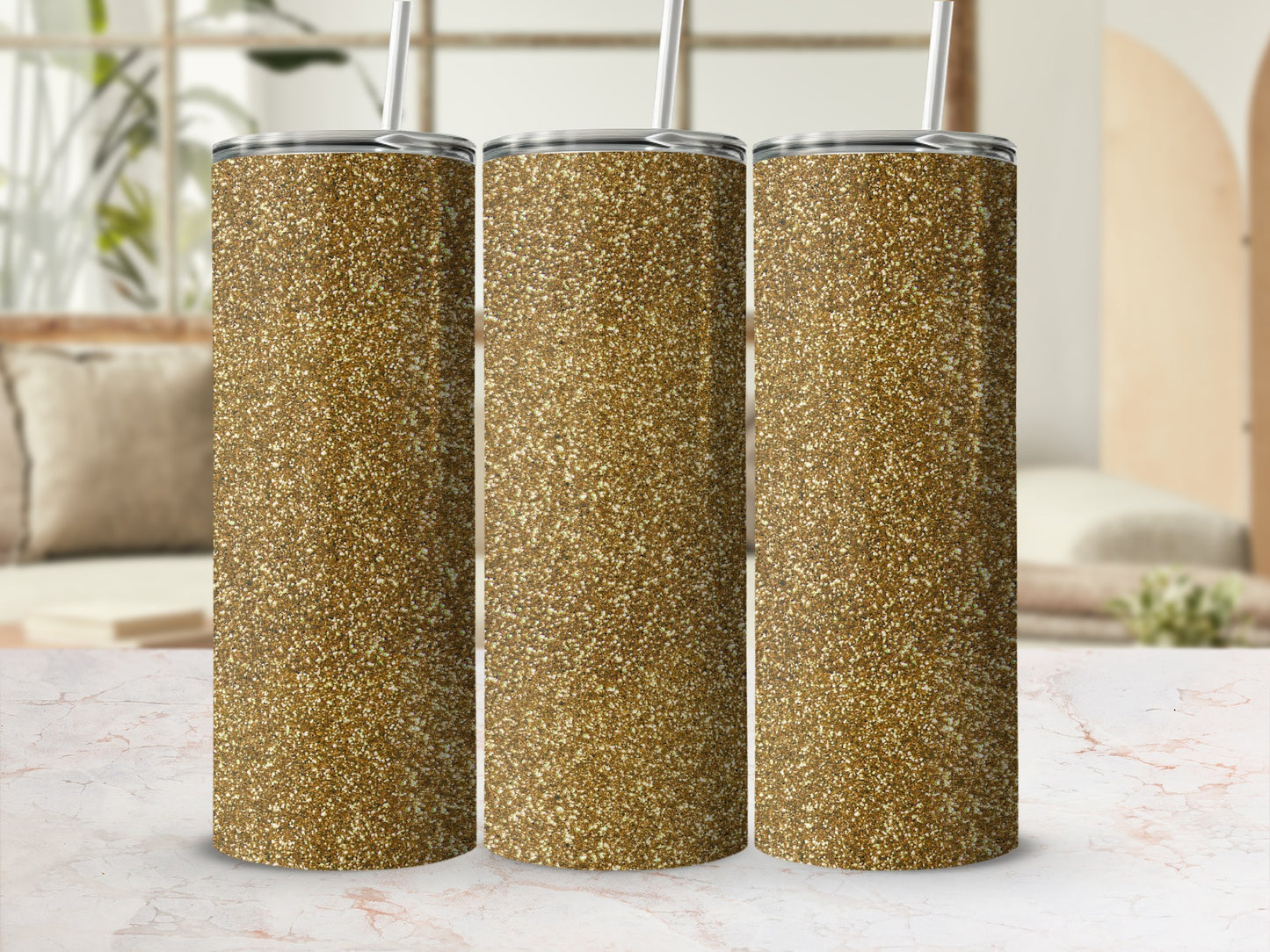 Three gold glitter tumblers with straws stand on a marble surface.