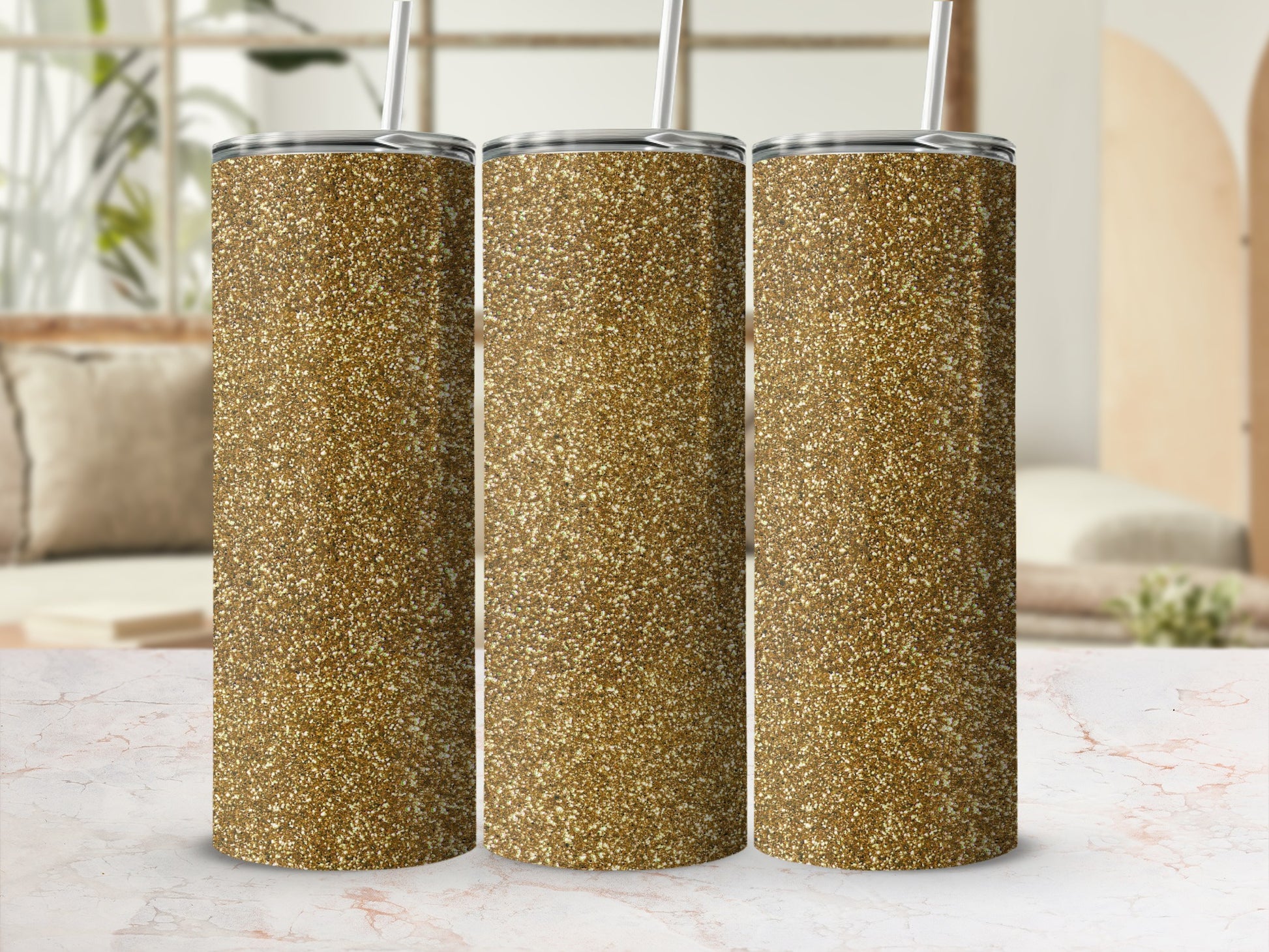 Three gold glitter tumblers with straws stand on a marble surface.