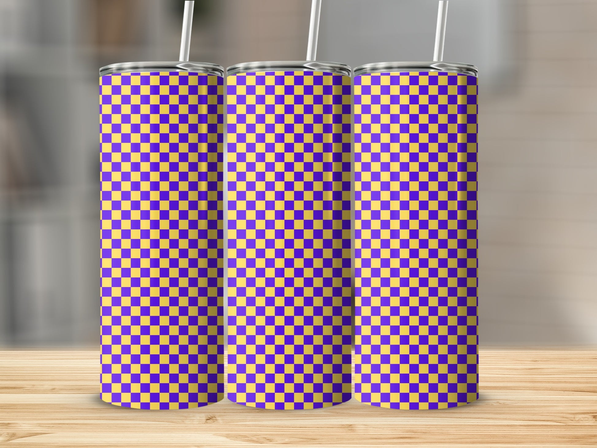 Three purple and yellow checkered tumblers with straws displayed on a wooden surface.