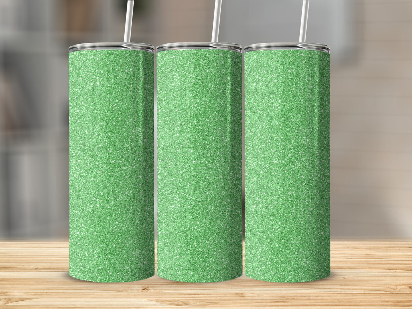 Three glitter green tumblers with white straws stand on a wooden table.