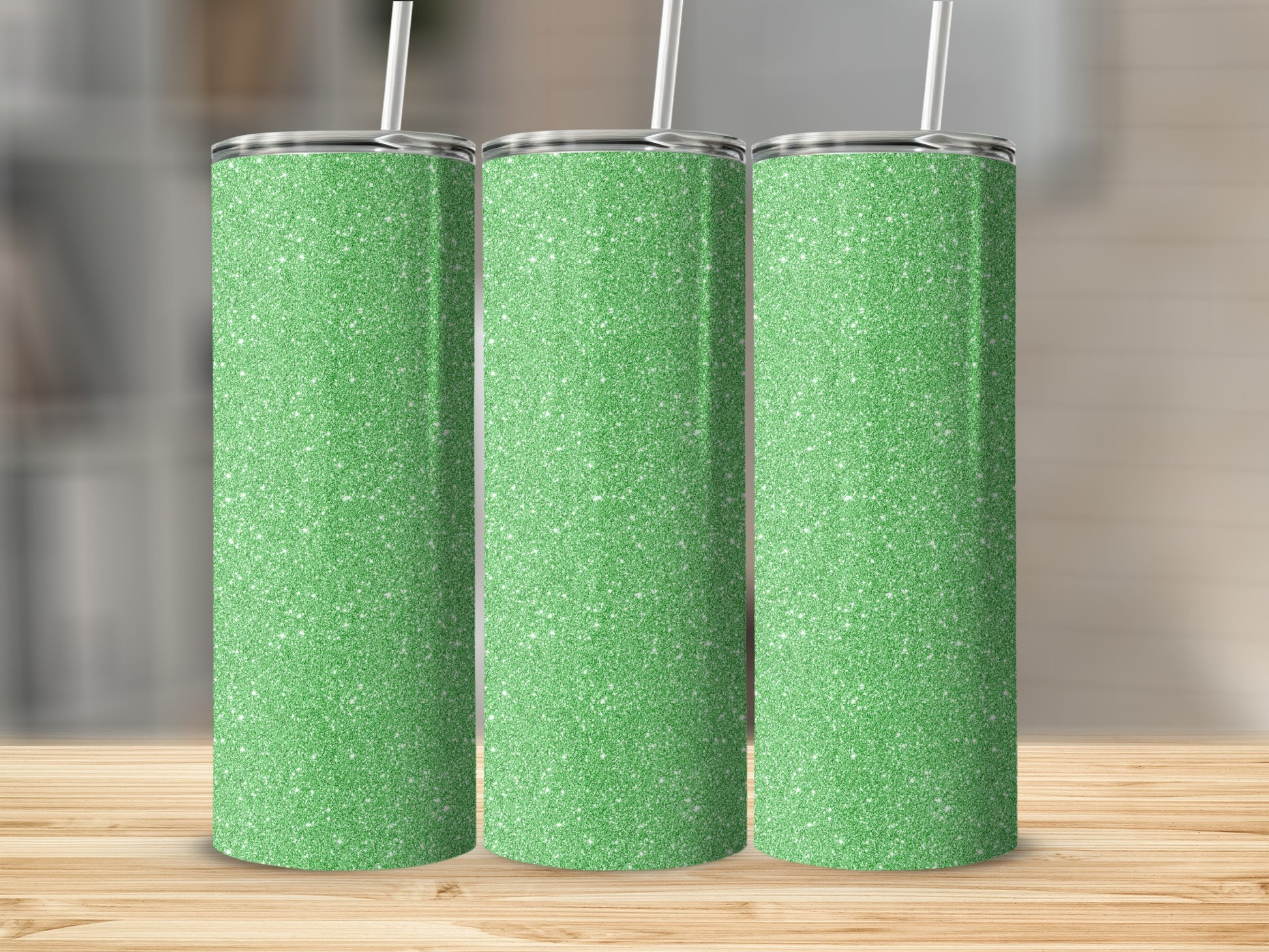 Three glitter green tumblers with white straws stand on a wooden table.