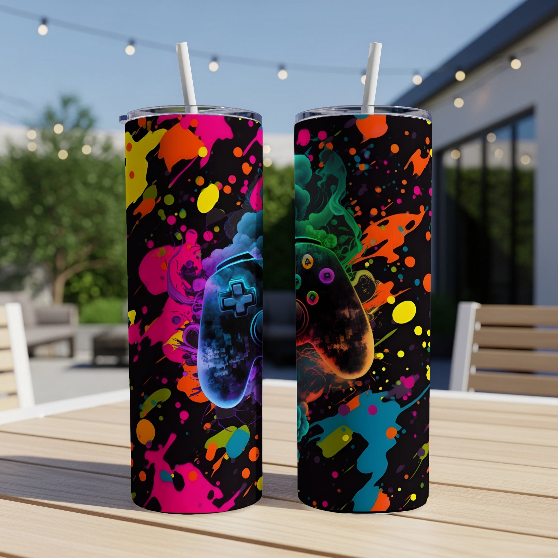 Two tumblers with colorful paint splatters and game controllers on a table.