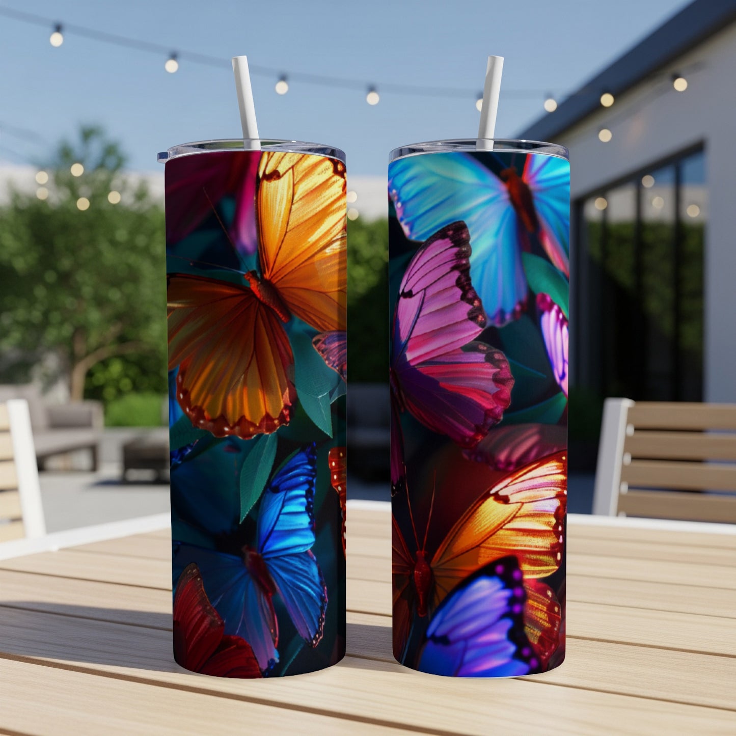 Two colorful butterfly print tumblers with straws on a table outdoors.