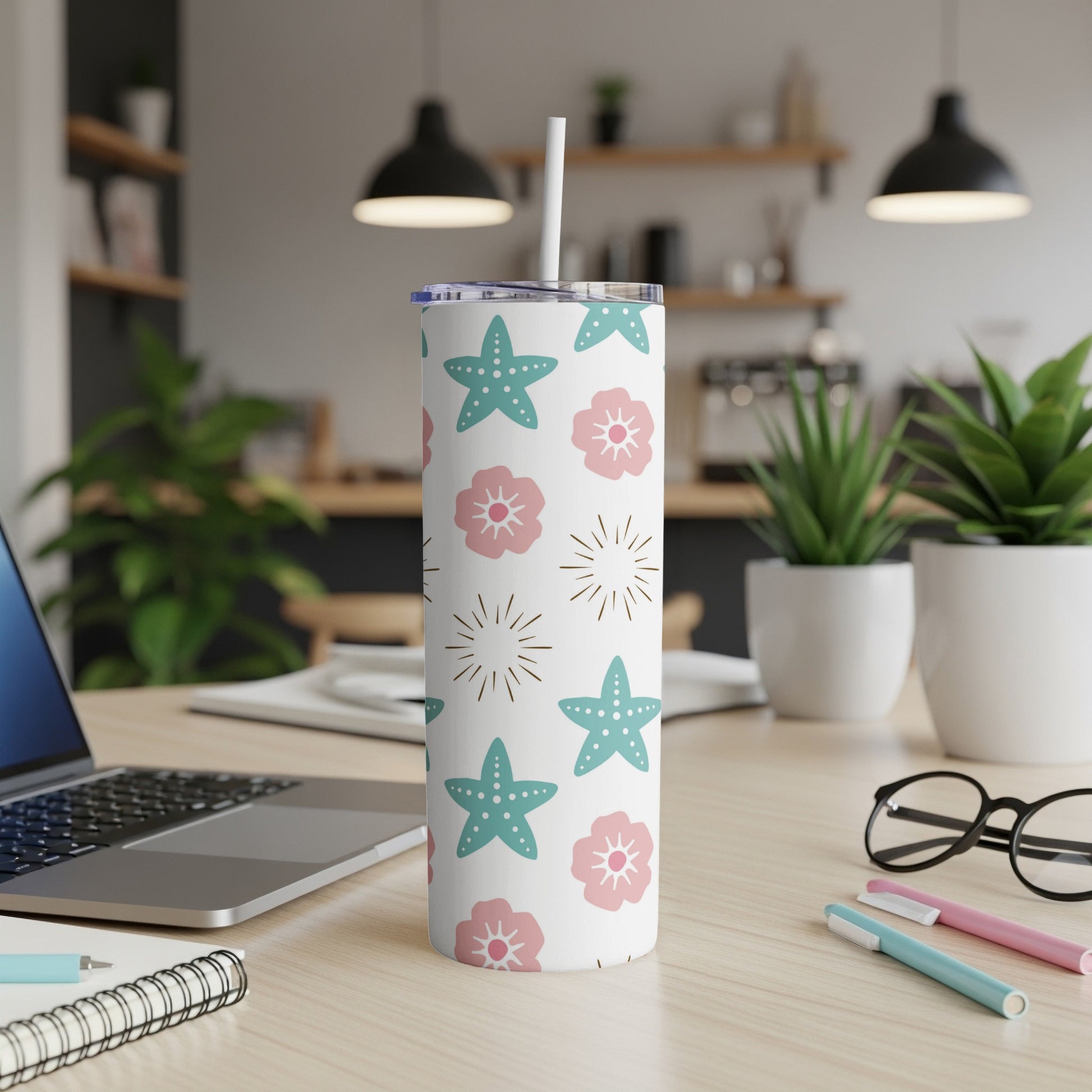 Teal tumbler with starfish and floral pattern, straw inserted.
