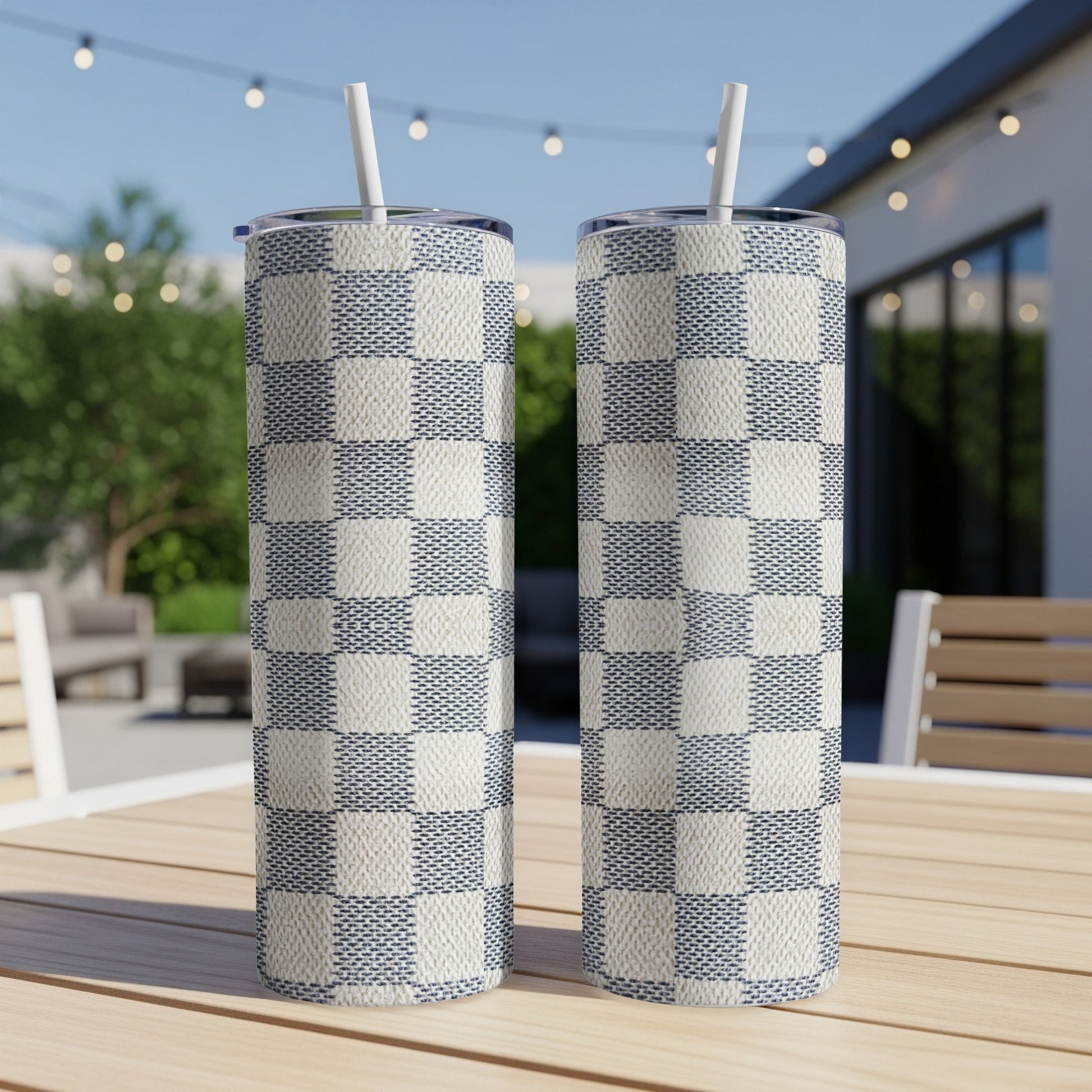 Two checkered pattern tumblers with straws on a wooden table outdoors.