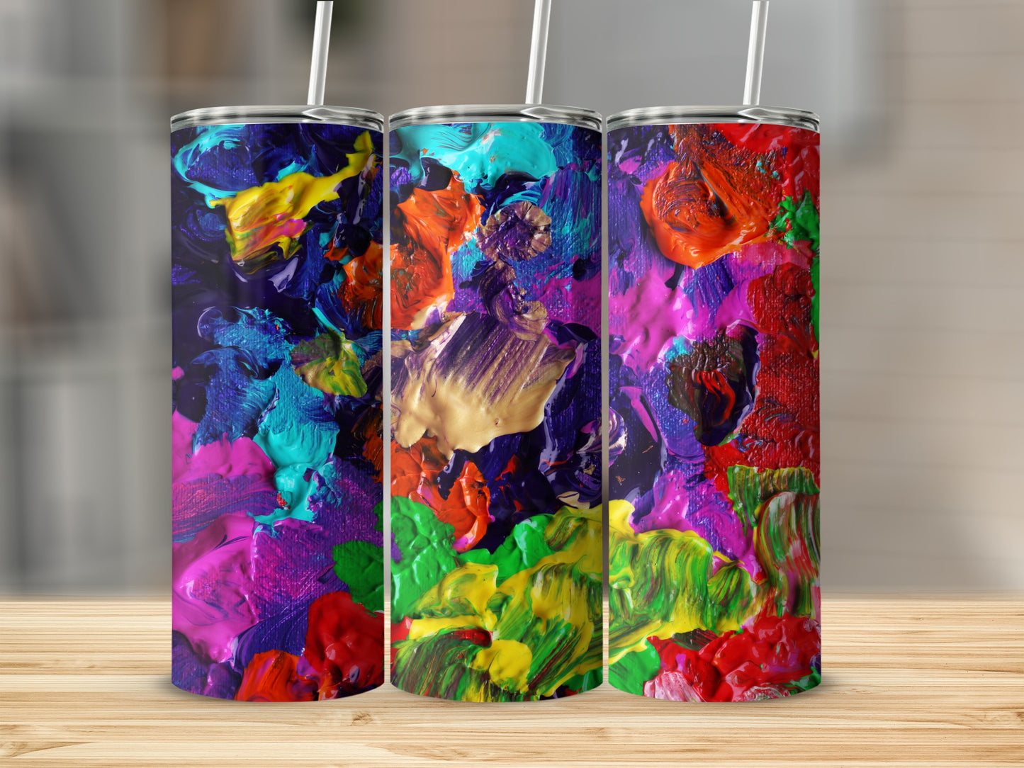 Three colorful tumblers with abstract paint textures stand on a wooden surface.