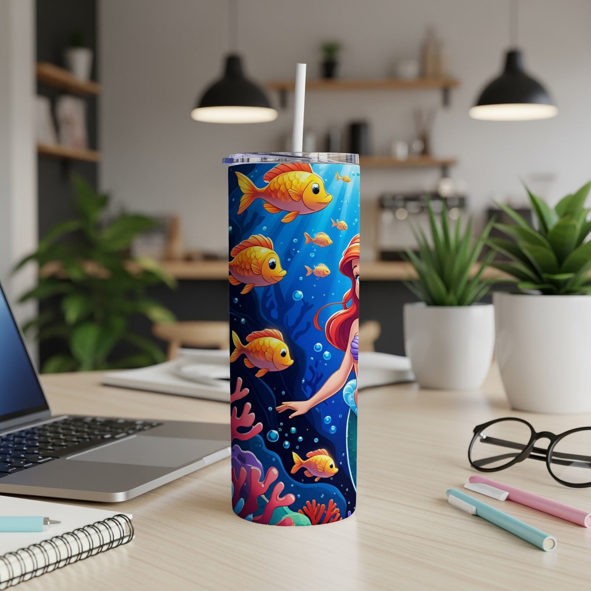 Mermaid and fish on a tumbler on a desk with laptop and pens.