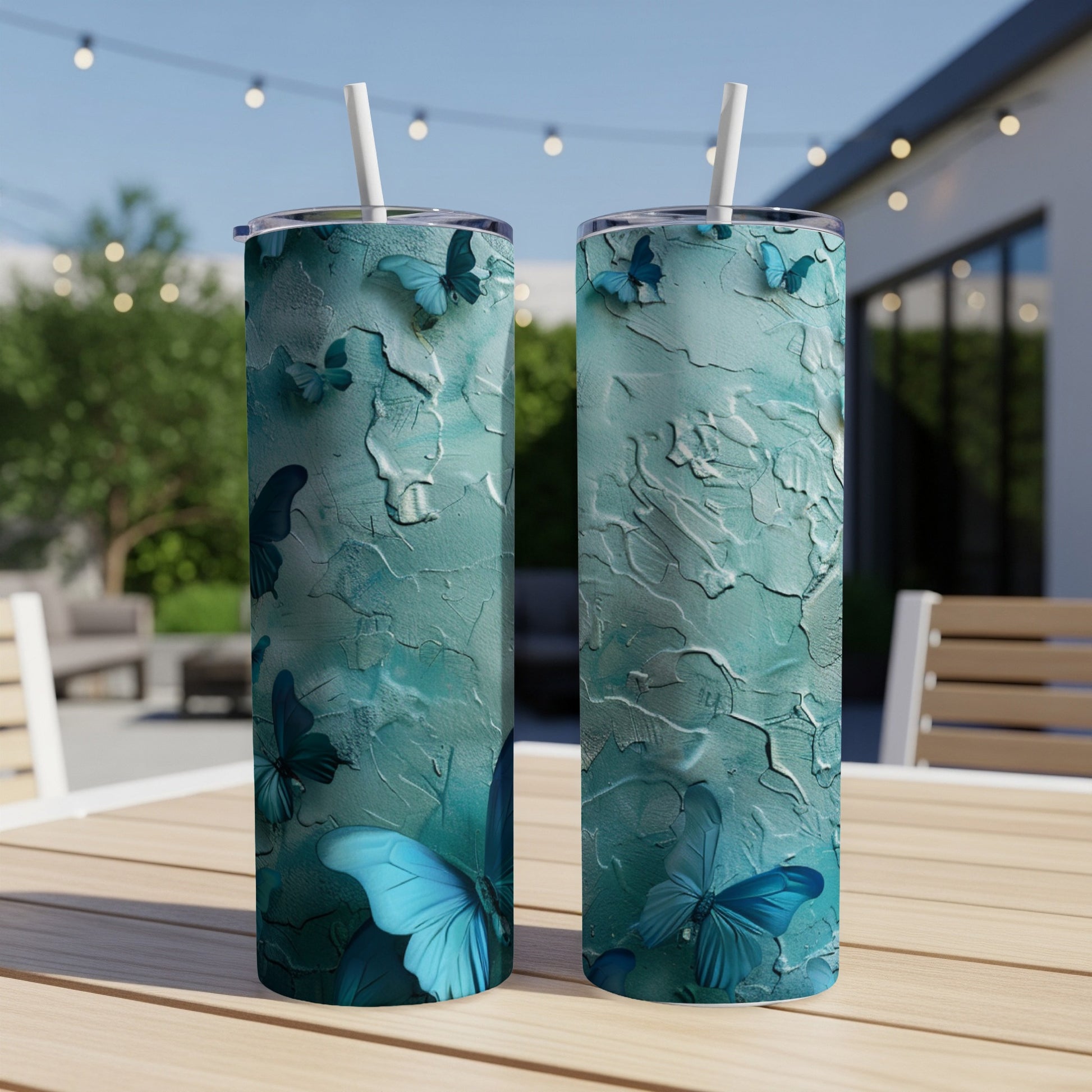 Two teal tumblers with textured butterfly design on an outdoor table.