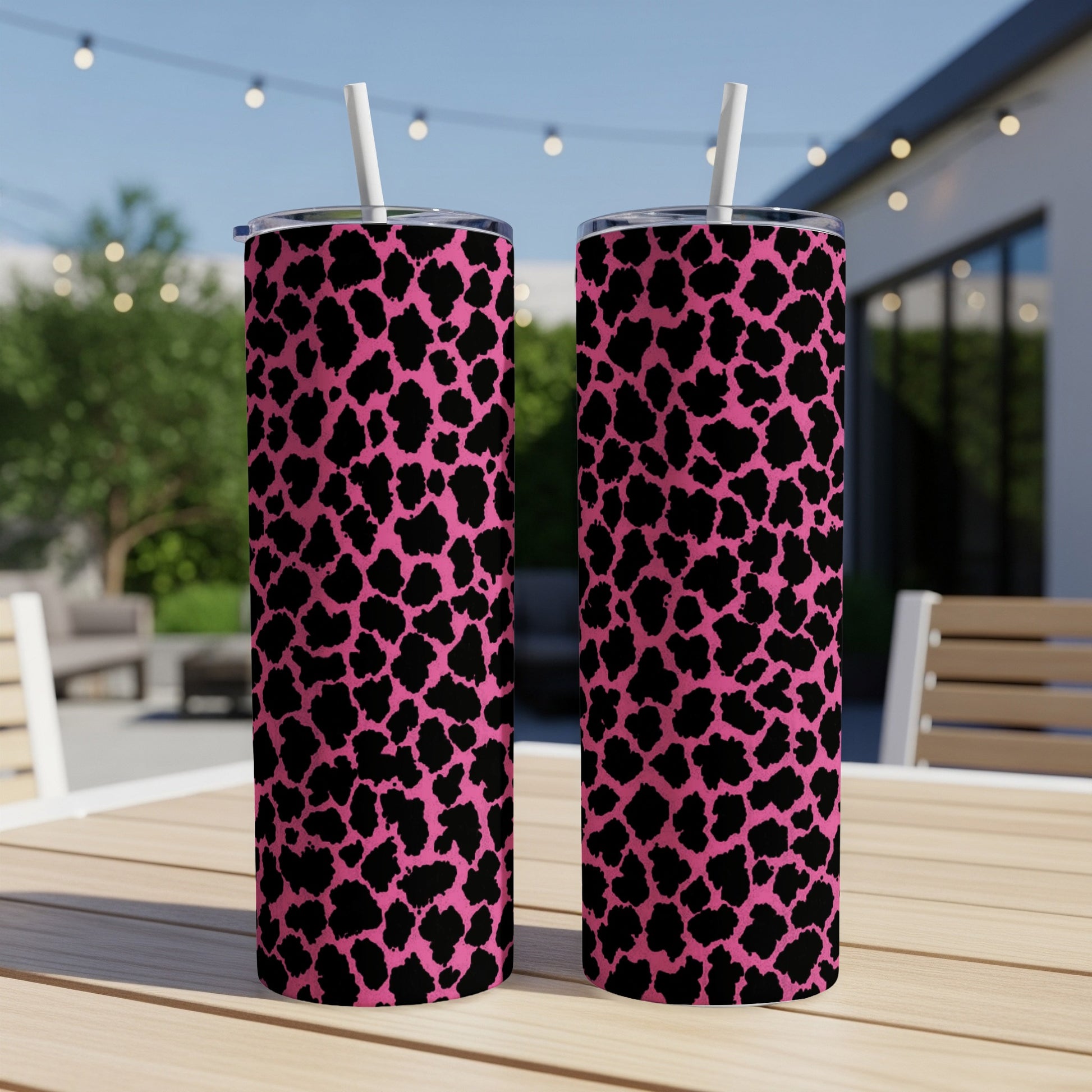 Two pink tumblers with black leopard print and white straws on a wooden table.