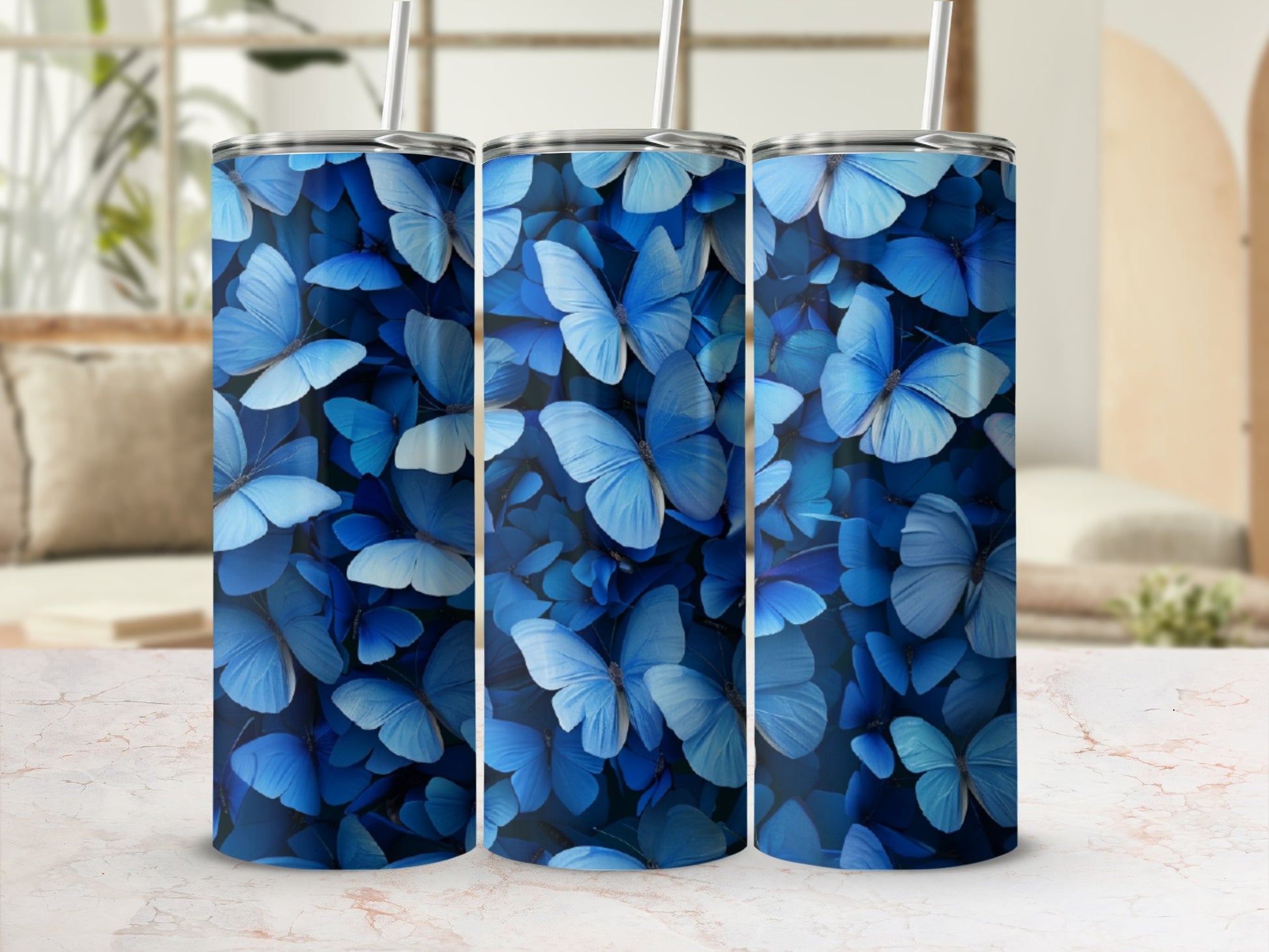 Three blue butterfly patterned tumblers with straws on a marble surface.