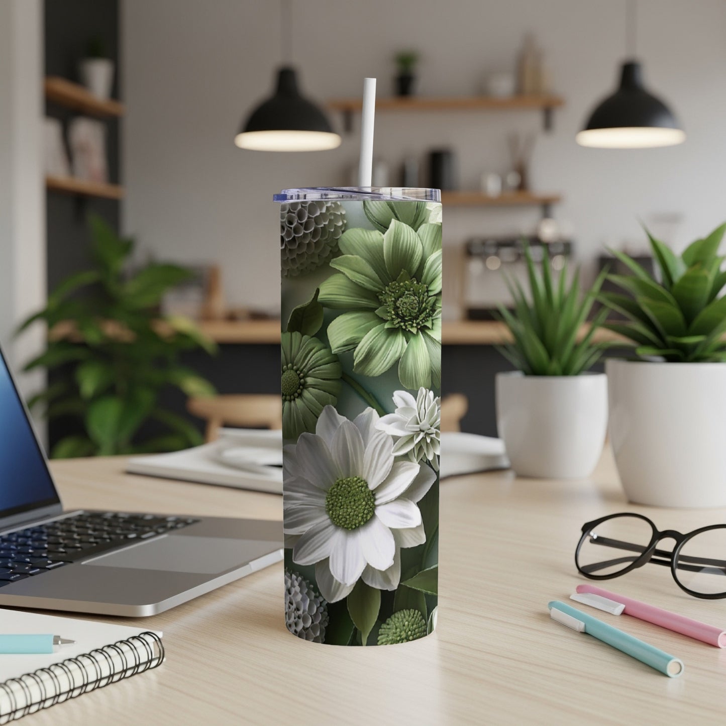 Green floral patterned tumbler with straw on desk beside laptop and pens.