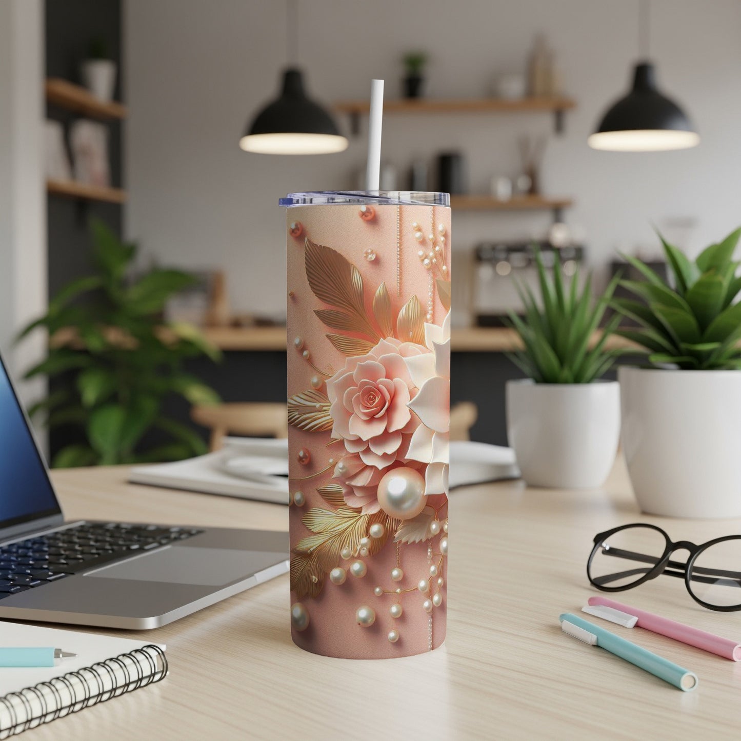 Pink floral tumbler with gold accents and pearls, on a desk.