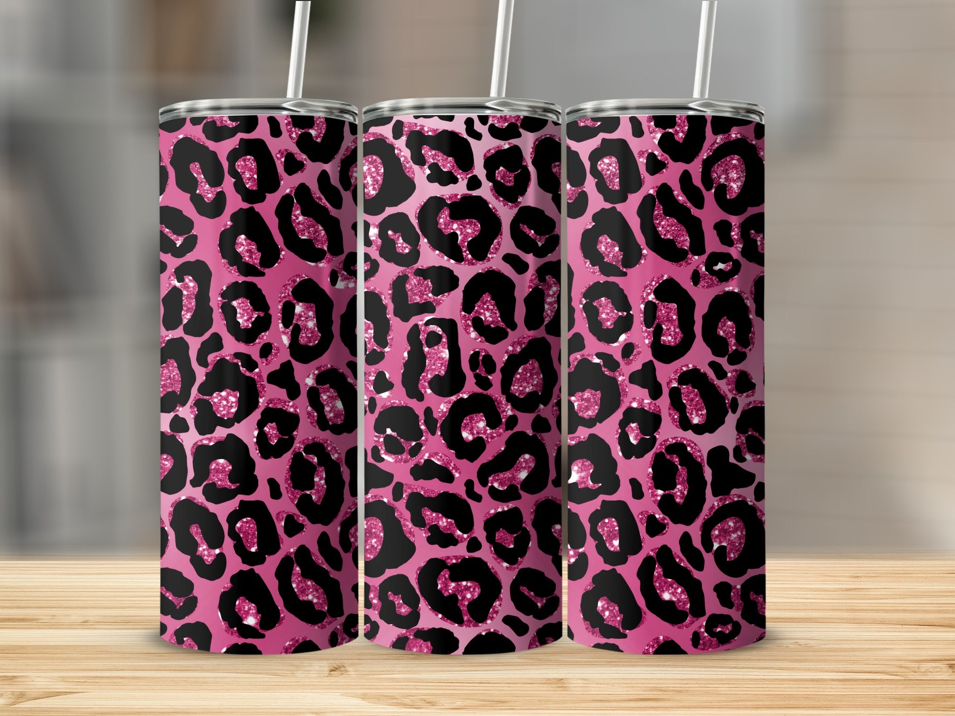 Three tumblers with pink leopard print and glitter details stand on a wooden surface.