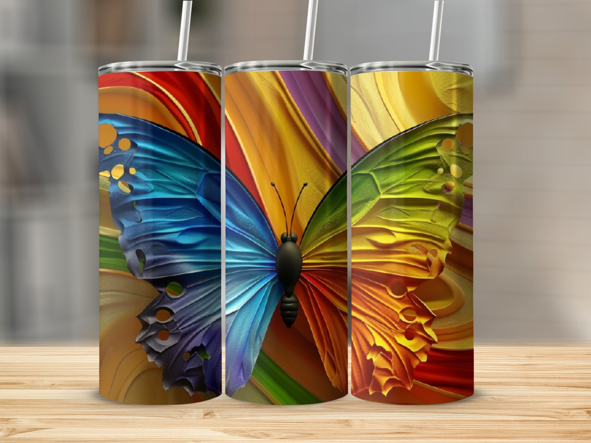 Three tumblers with vibrant butterfly wing designs and straws.