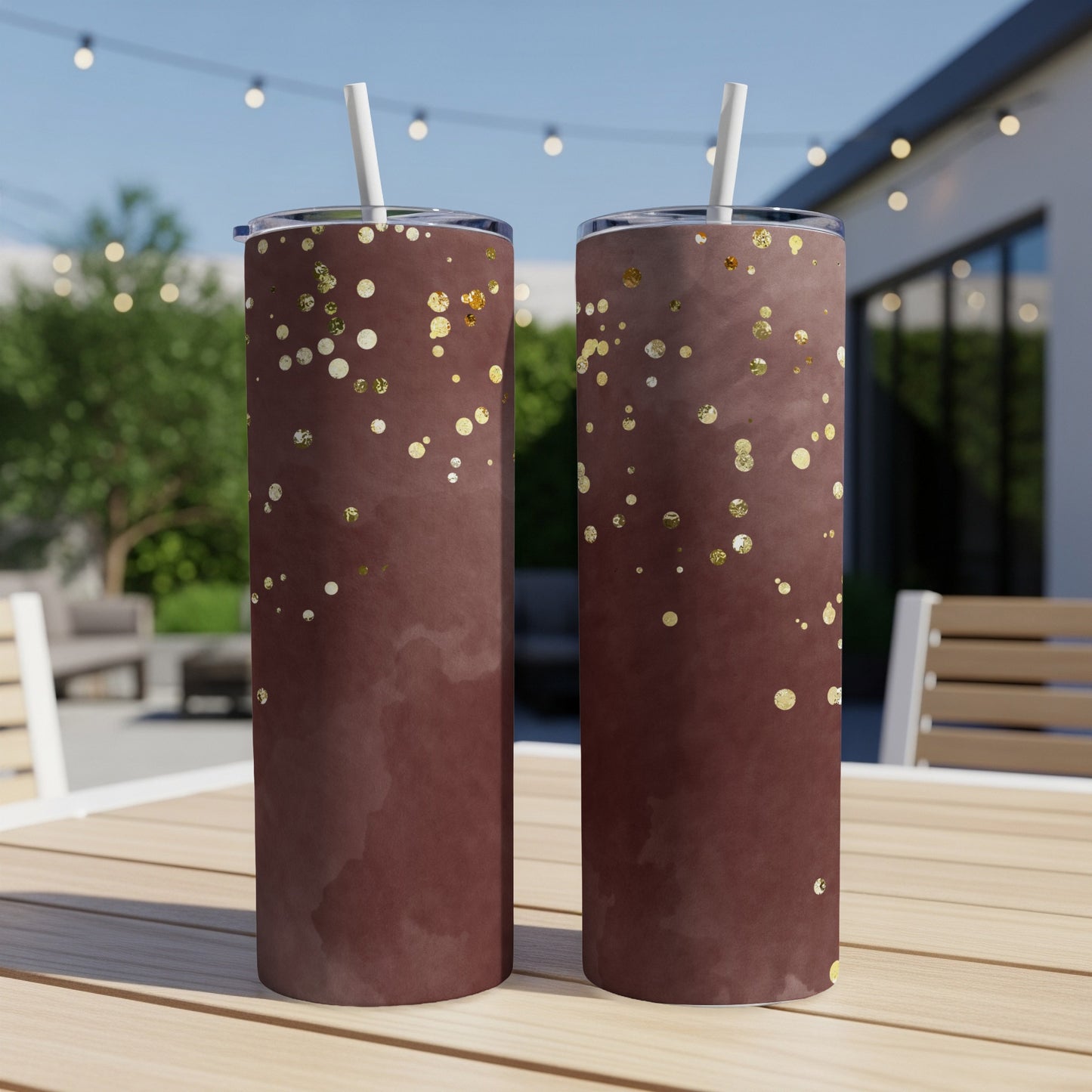 Two brown tumblers with gold glitter dots sit on a wooden table outdoors.