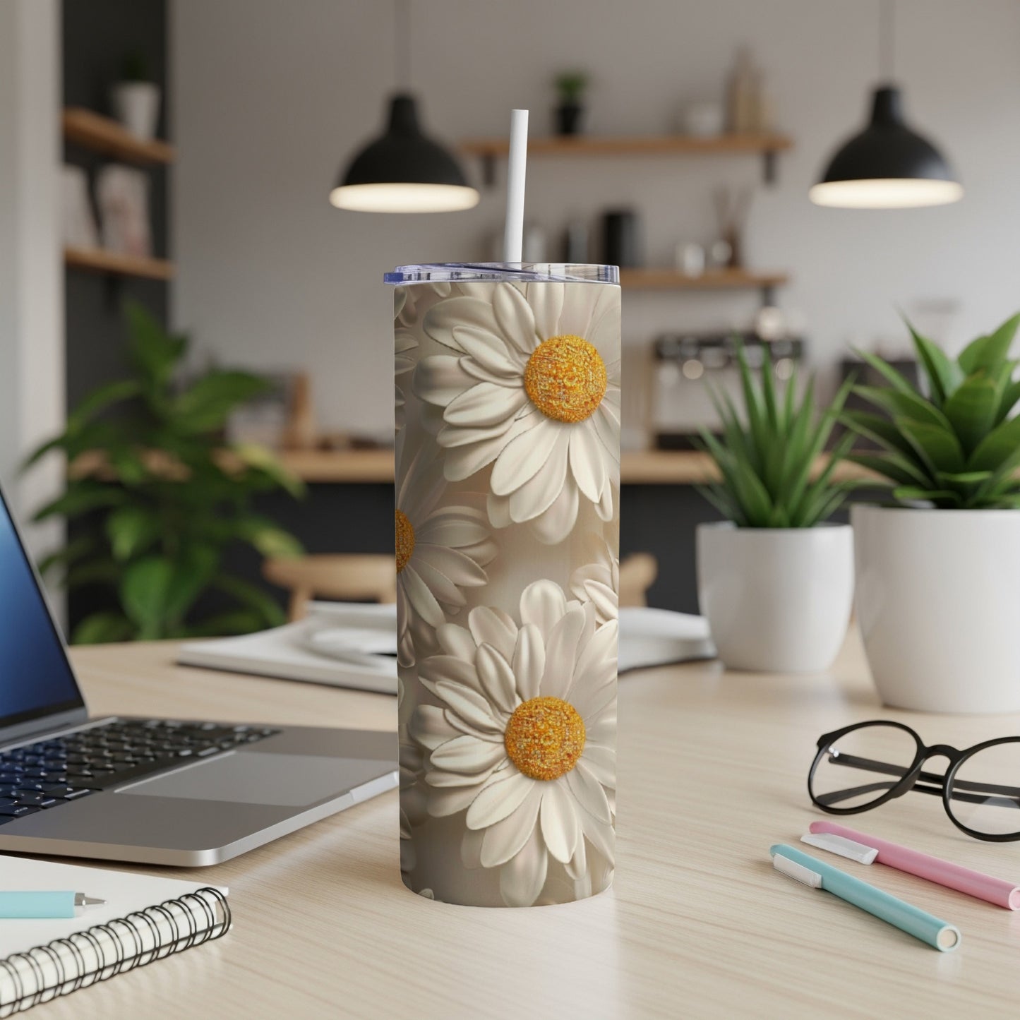 Tall tumbler with white daisies and a straw on a desk.