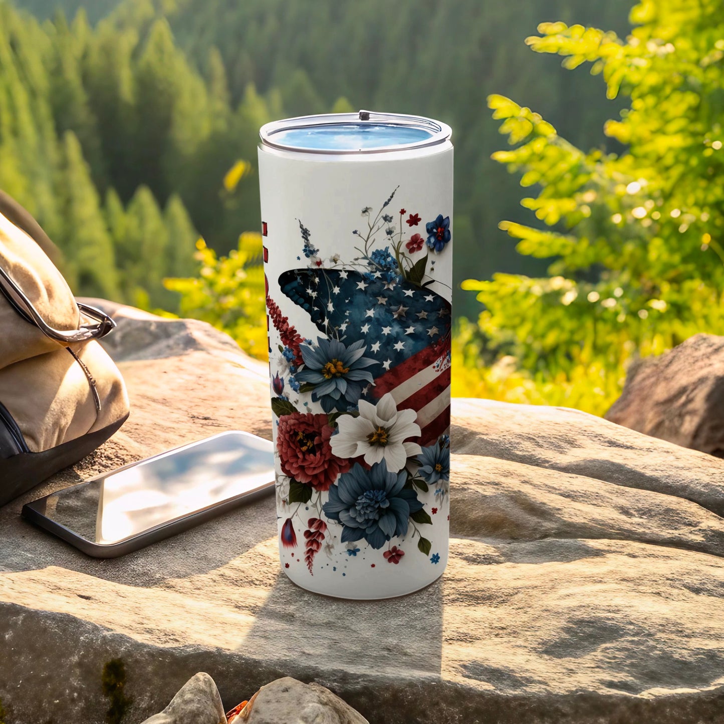 White tumbler with American flag floral design outdoors on rock.