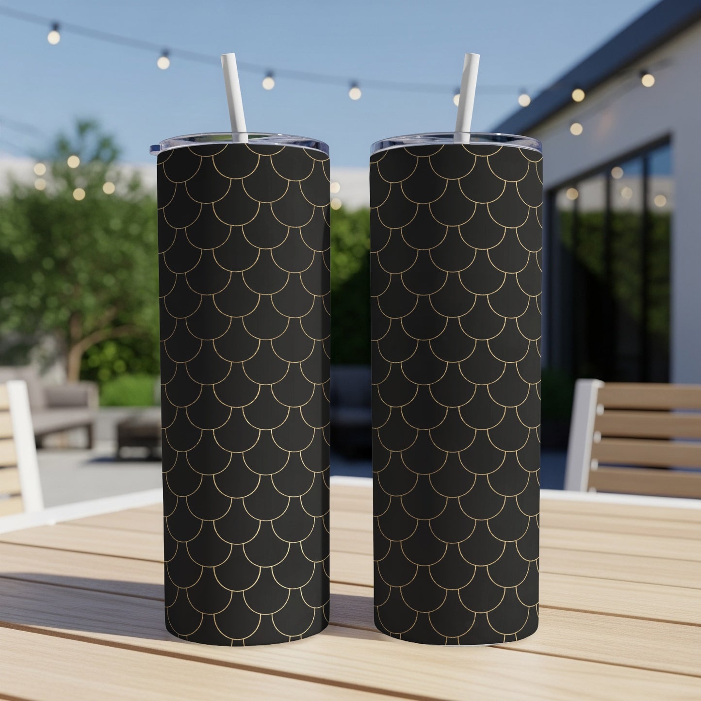 Two black tumblers with gold scaly design and white straws sit on a table.