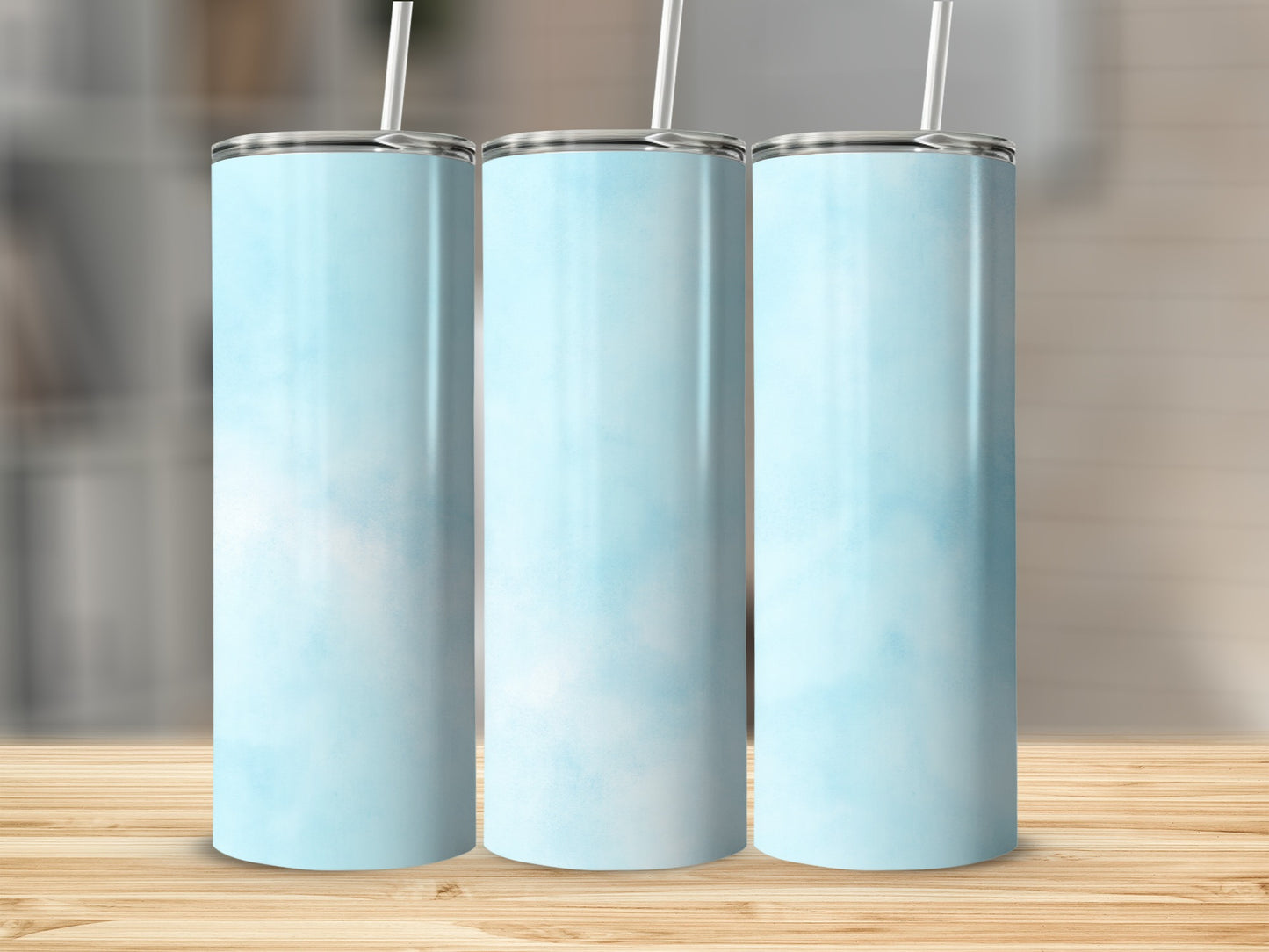 Three blue watercolor tumblers with white straws on a wooden surface.