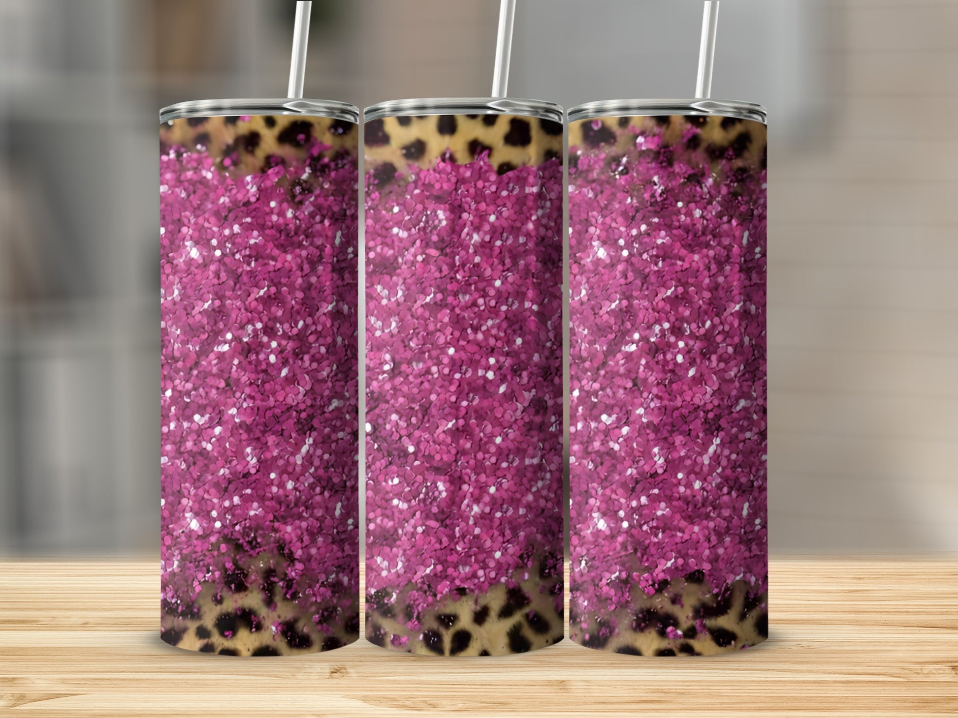 Pink glitter and leopard print tumbler with straw on wooden surface.