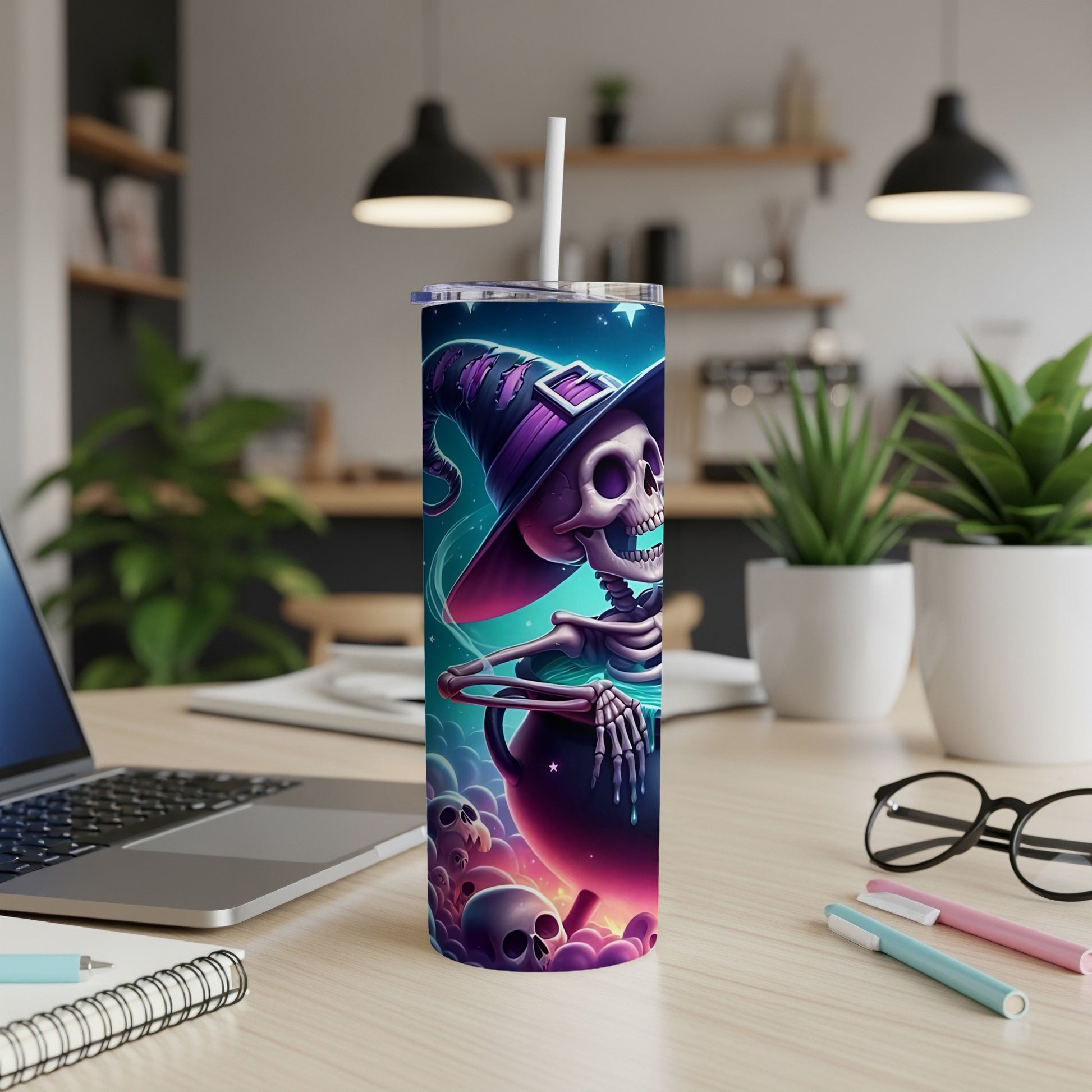Tumbler with skeleton witch, cauldron, and skulls graphic on a desk.