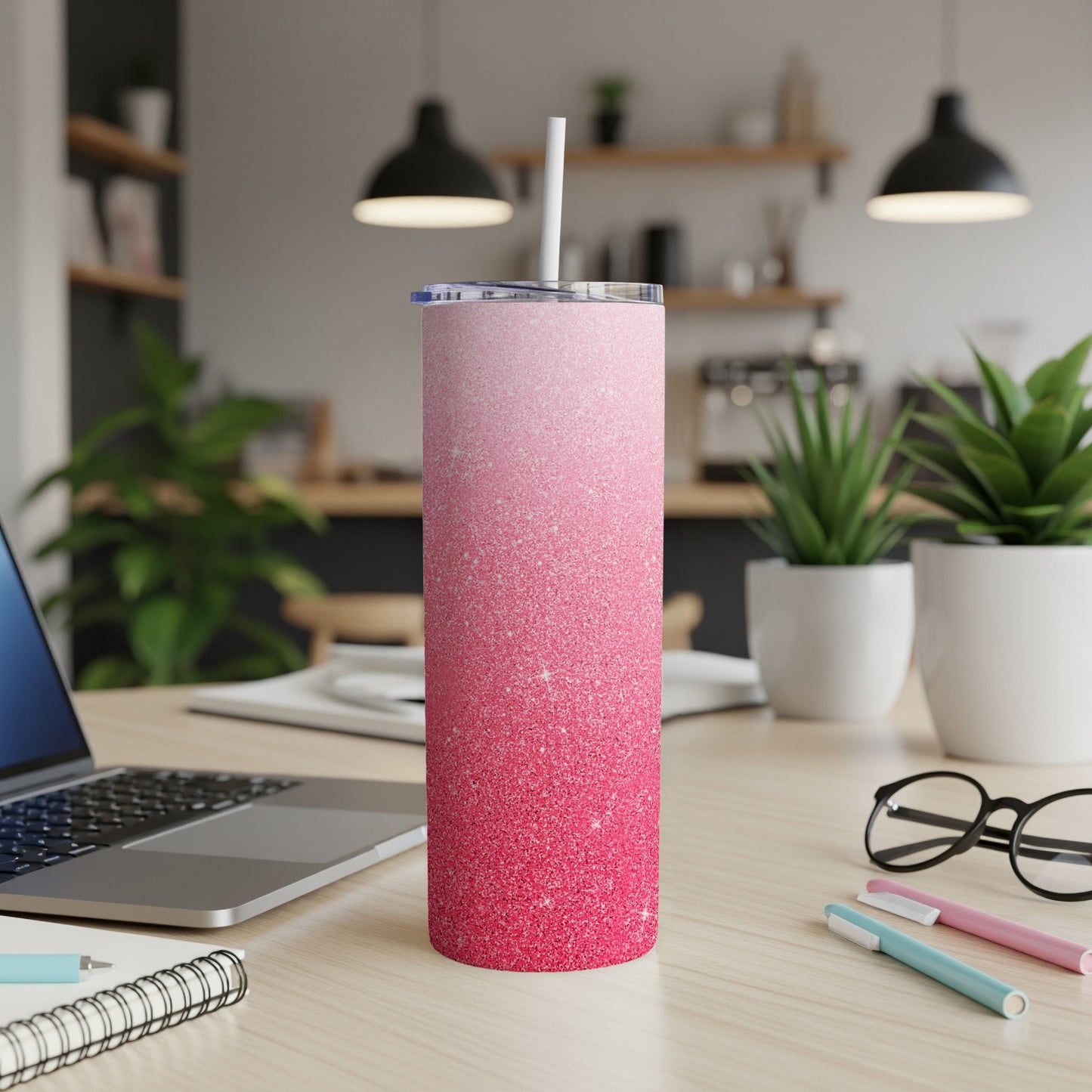 Pink glitter tumbler with straw on a desk, laptop, and plants.