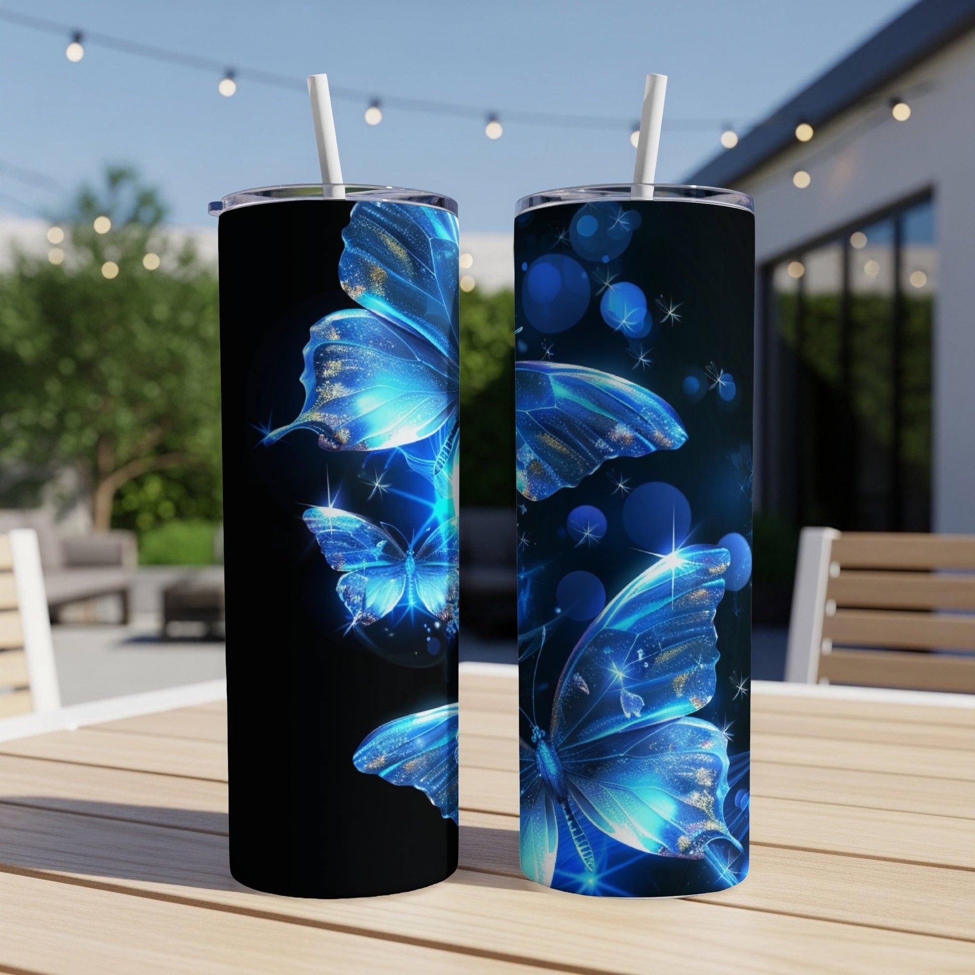 Two blue glittery butterfly tumblers with straws on a table outdoors.