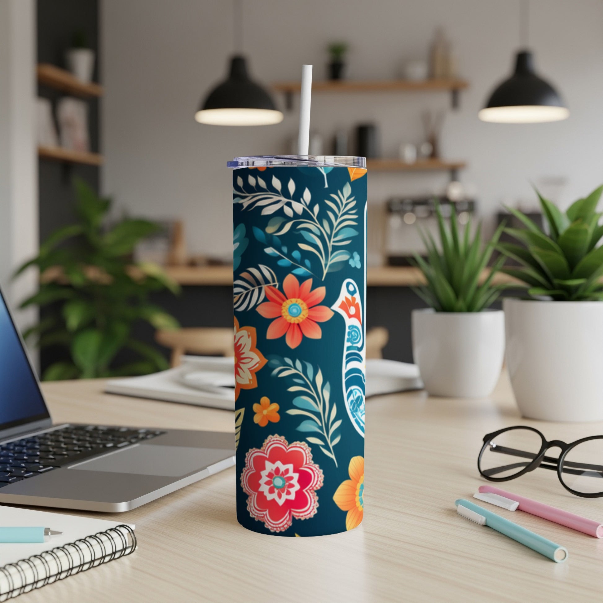 Dark blue tumbler with floral and bird pattern, straw in lid, on a desk.