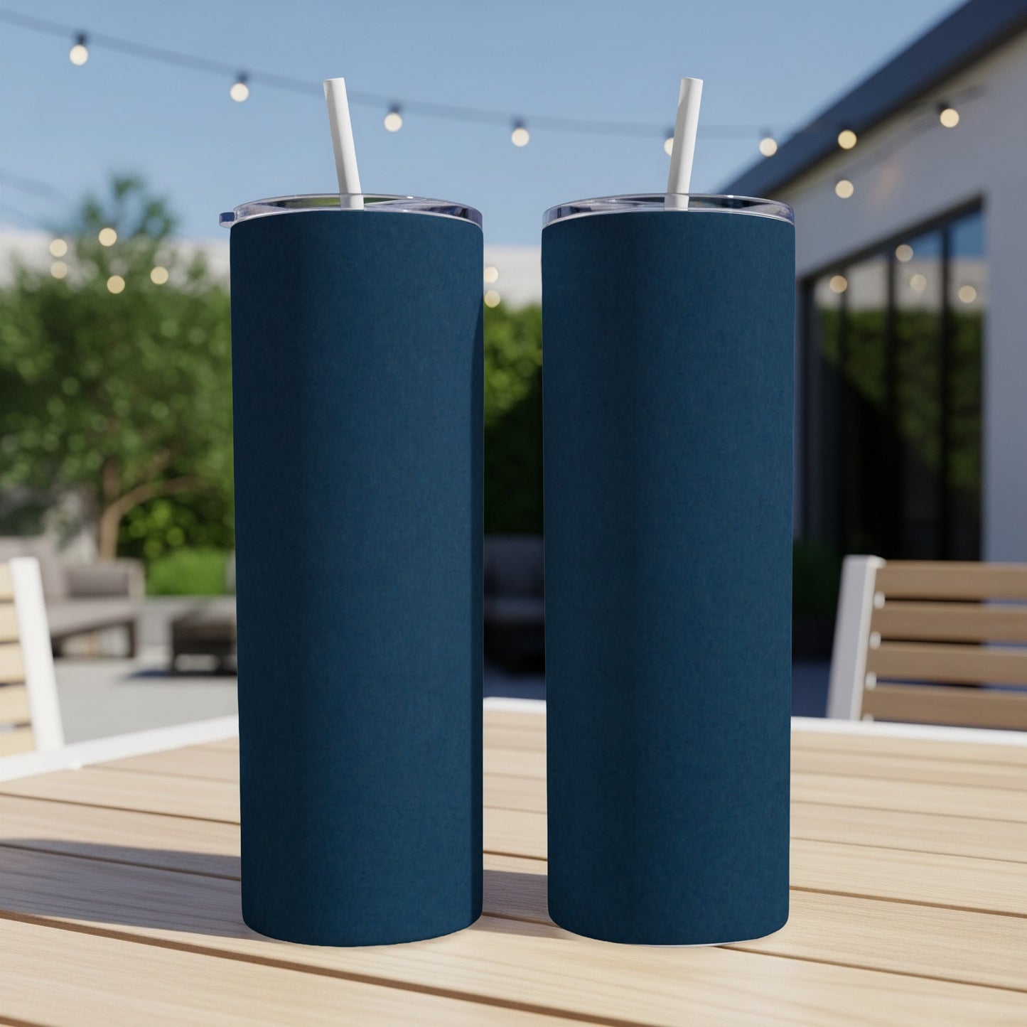 Two navy blue tumblers with white straws sit on a wooden table outdoors.