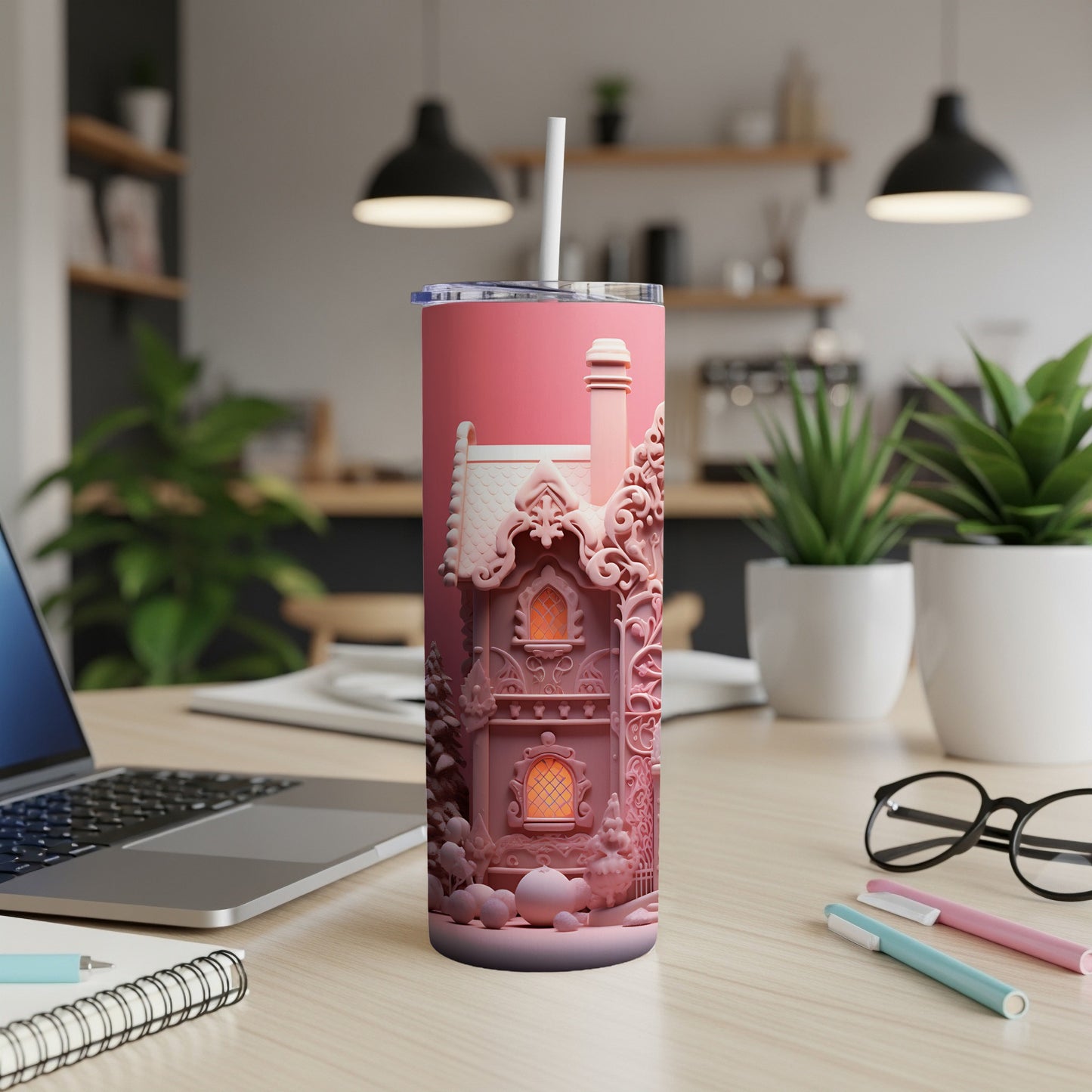 Pink tumbler with a whimsical house design and straw, on a desk.
