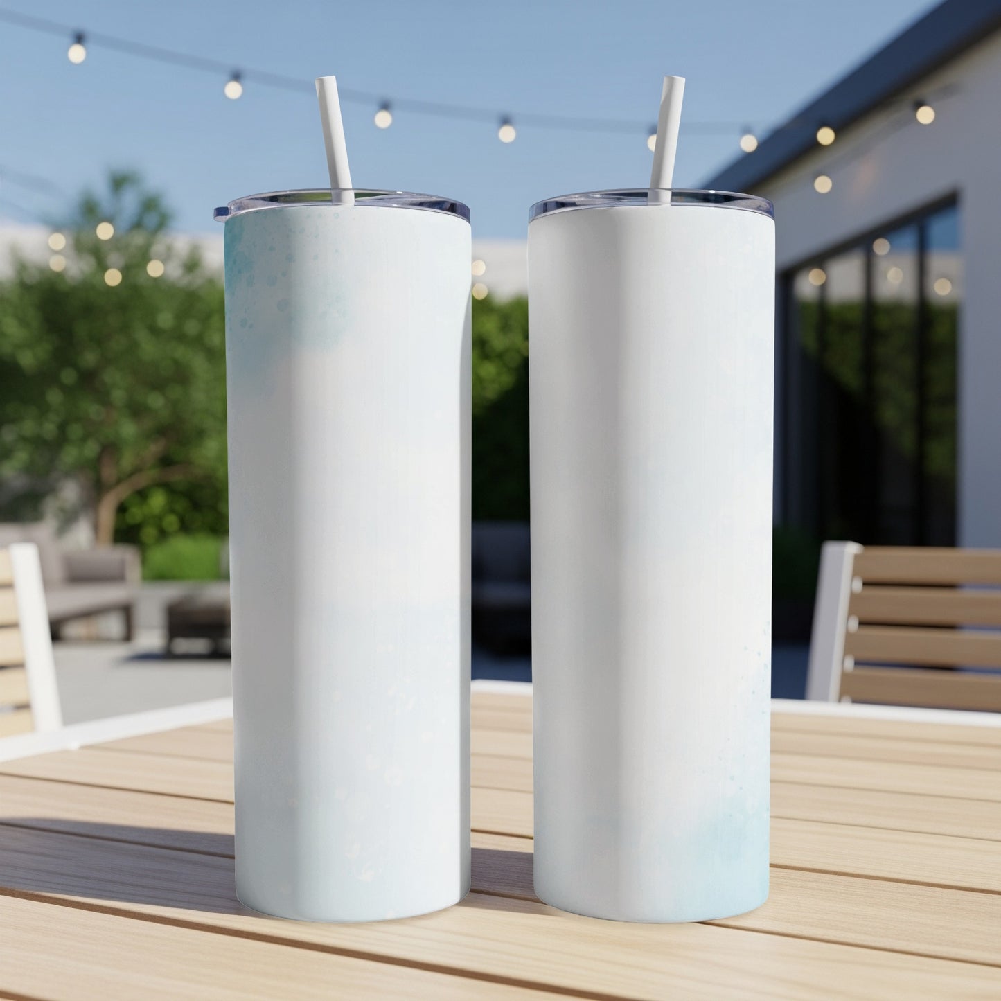 Two white tumblers with blue watercolor accents and straws on a wooden table.