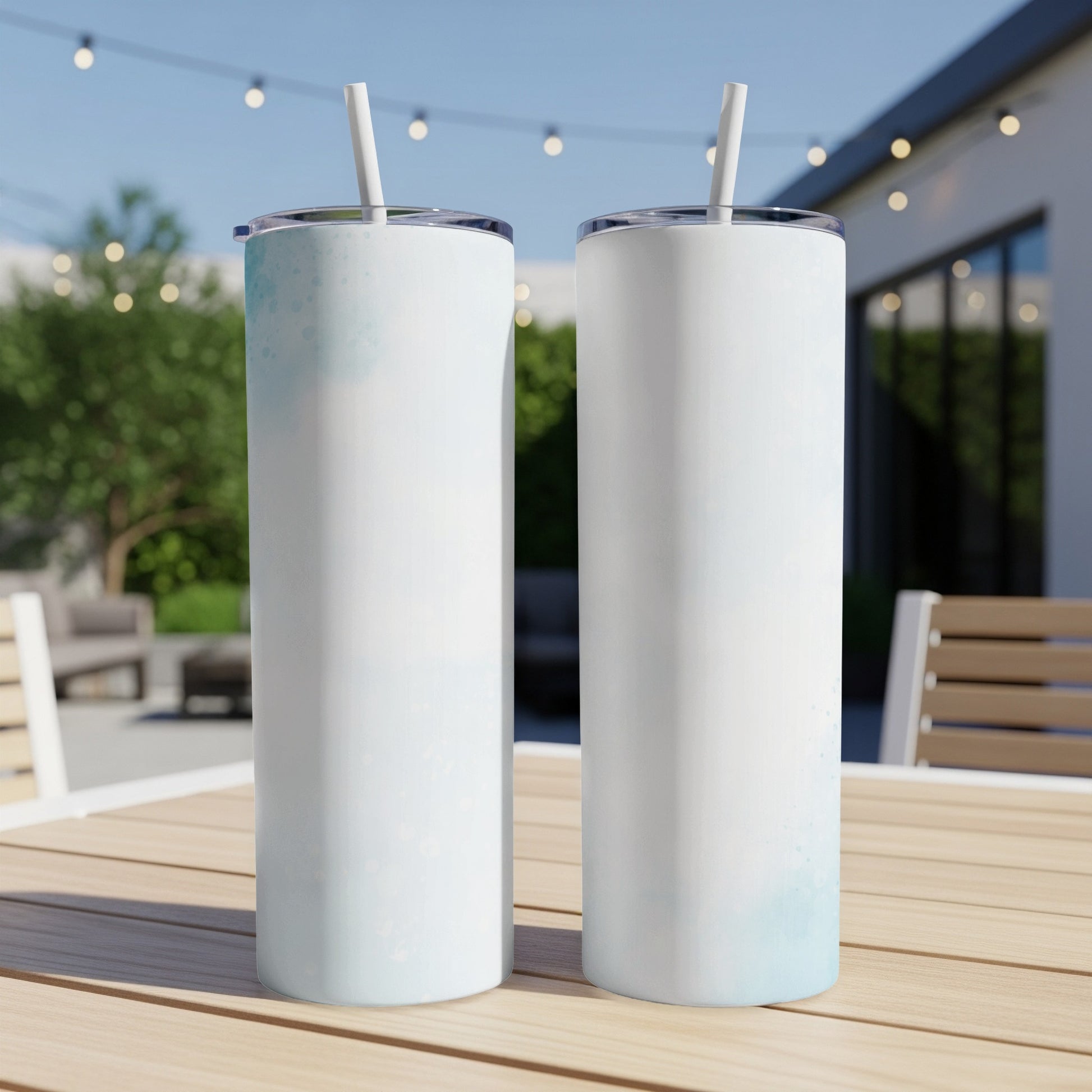 Two white tumblers with blue watercolor accents and straws on a wooden table.