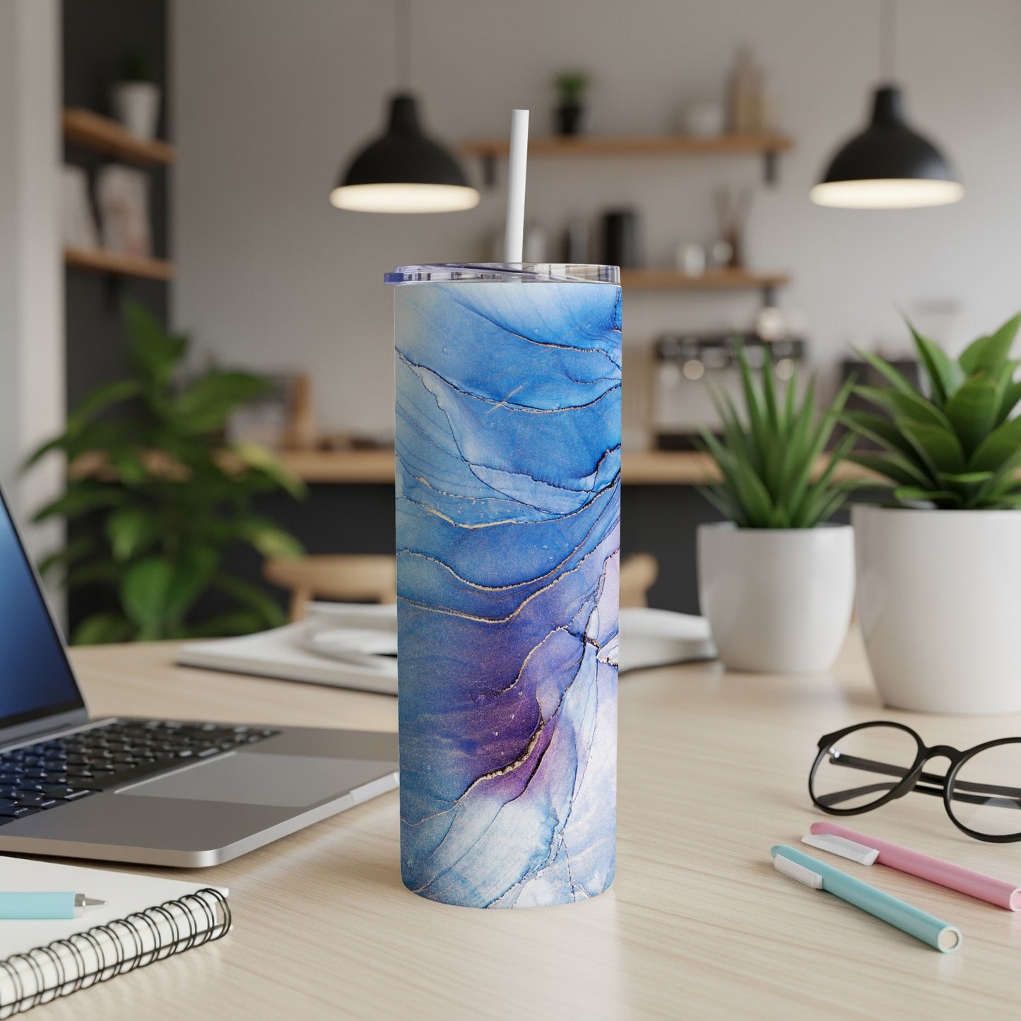 Blue, purple, and gold marble patterned tumbler with a straw on a desk.