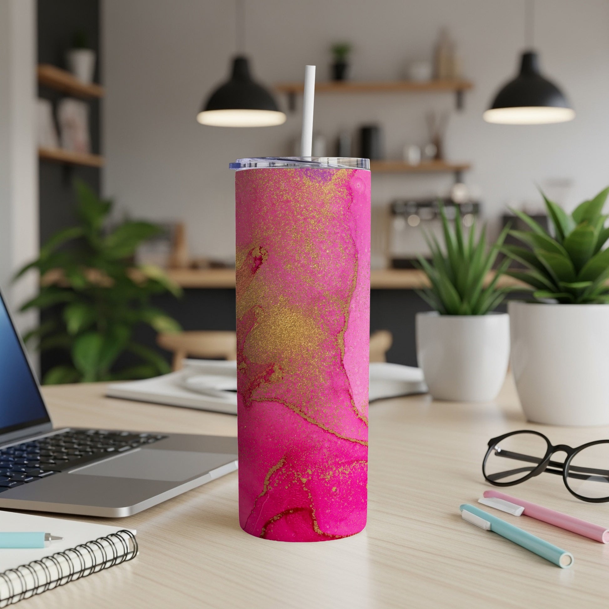 Pink and gold marbled skinny tumbler with straw on a desk.