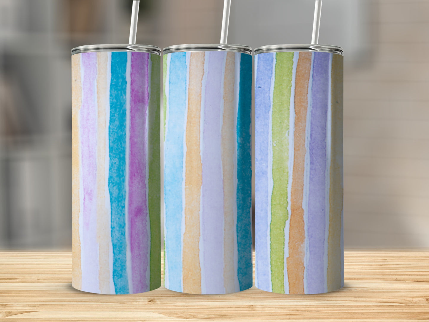 Three tumblers with colorful vertical watercolor stripes on a wooden surface.