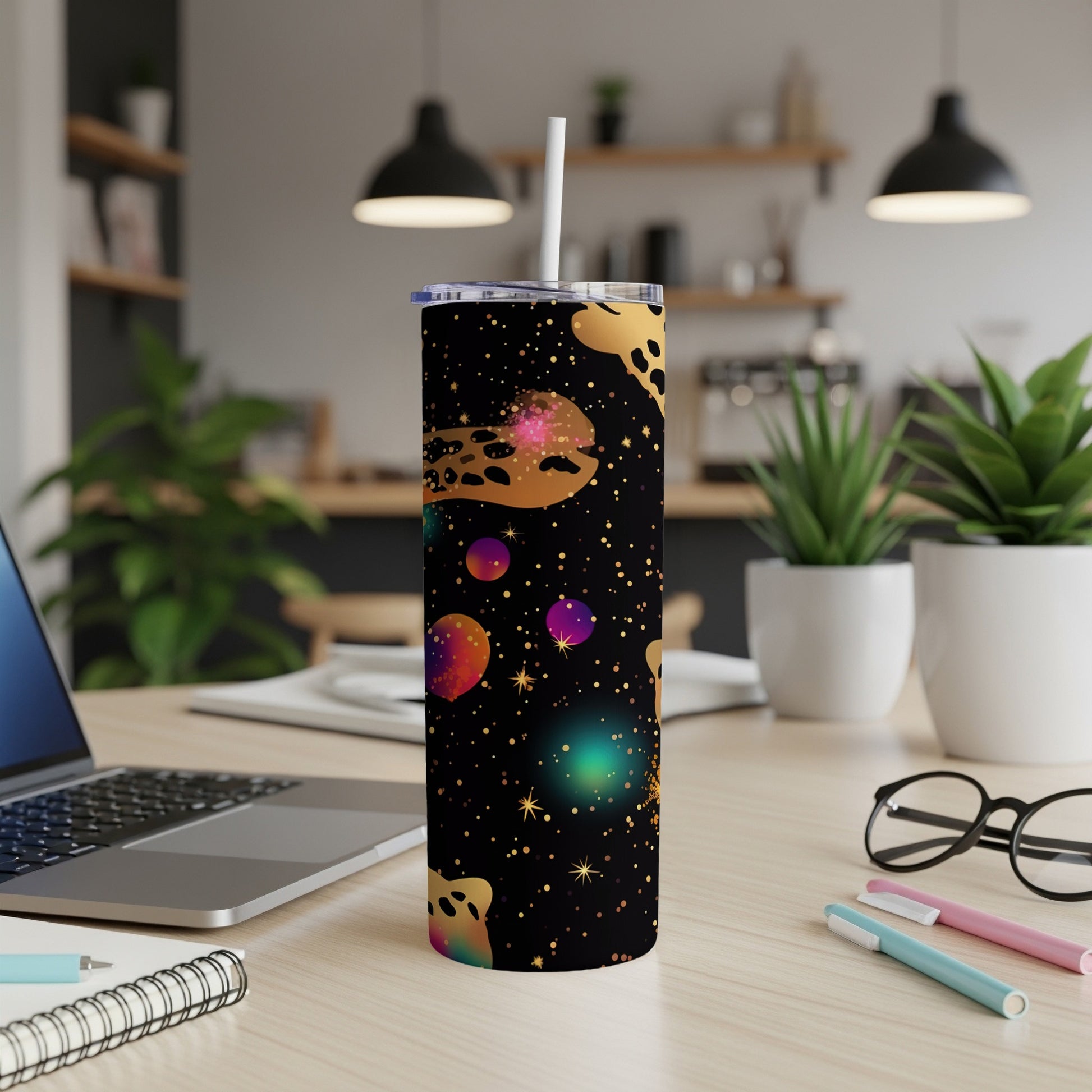 Black tumbler with colorful celestial pattern and straw, on a desk.