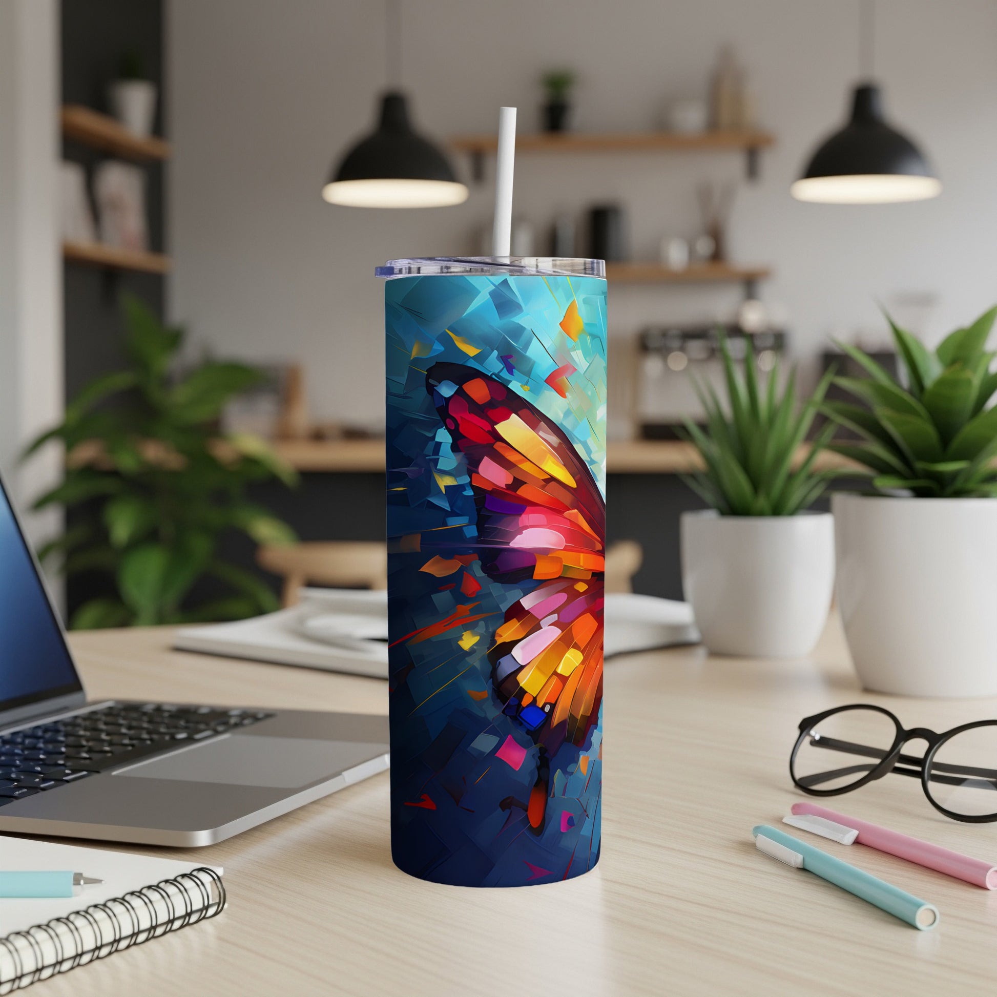 Tumbler with abstract butterfly wing design and white straw on desk.