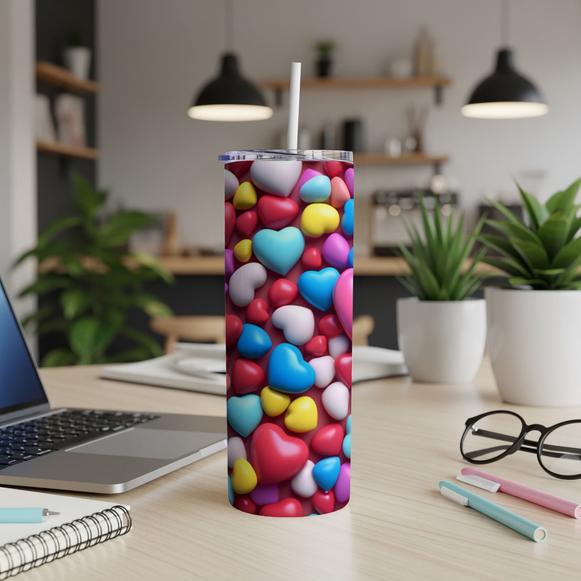Tall tumbler with scattered colorful hearts, straw, and laptop on desk.