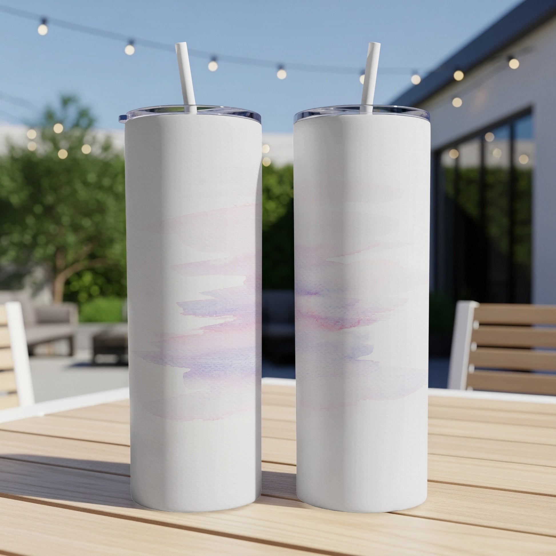 Two white tumblers with abstract watercolor brushstrokes on a wooden table outdoors.