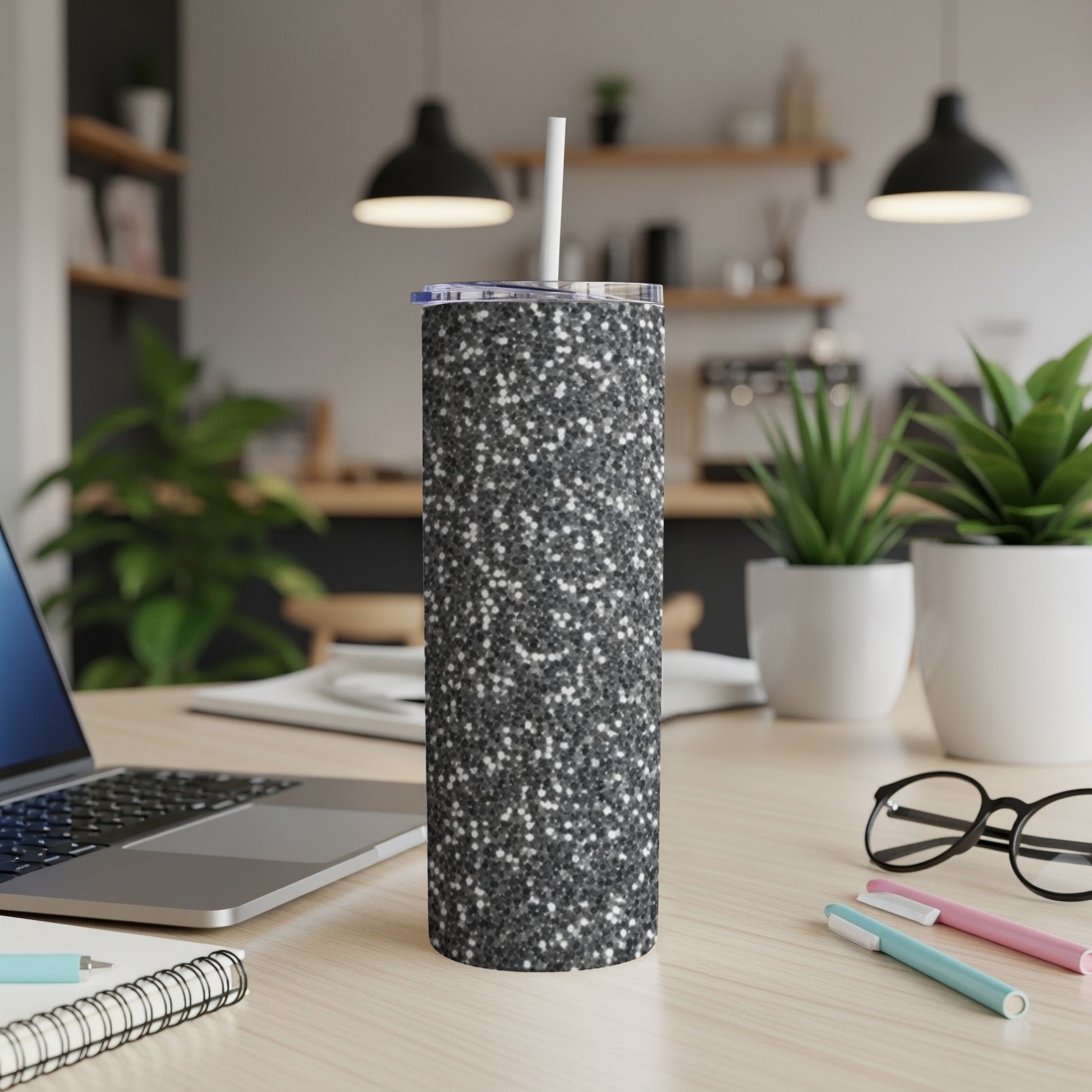 Glittery black tumbler with straw on a desk next to a laptop.
