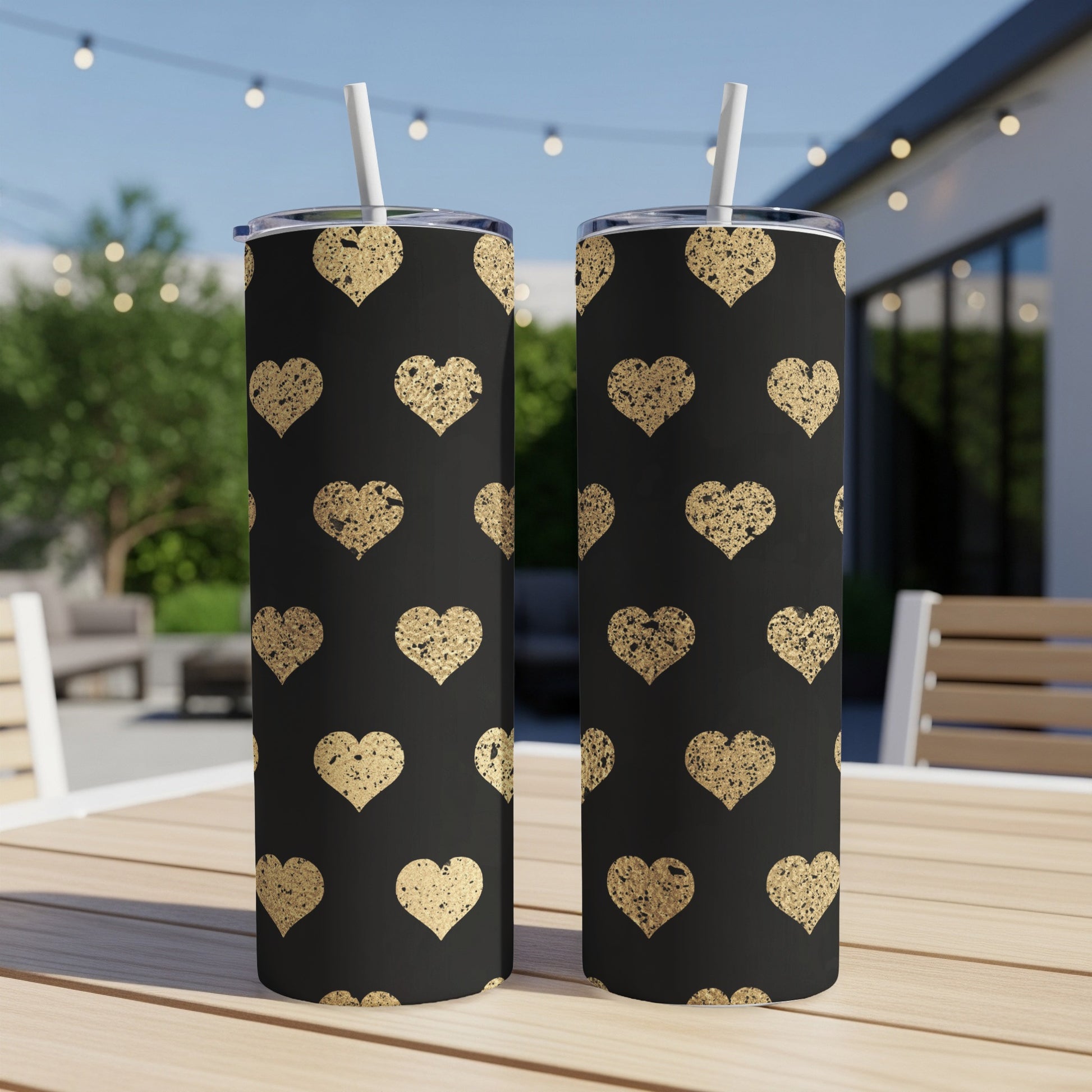 Two black tumblers with a gold distressed heart pattern and white straws.