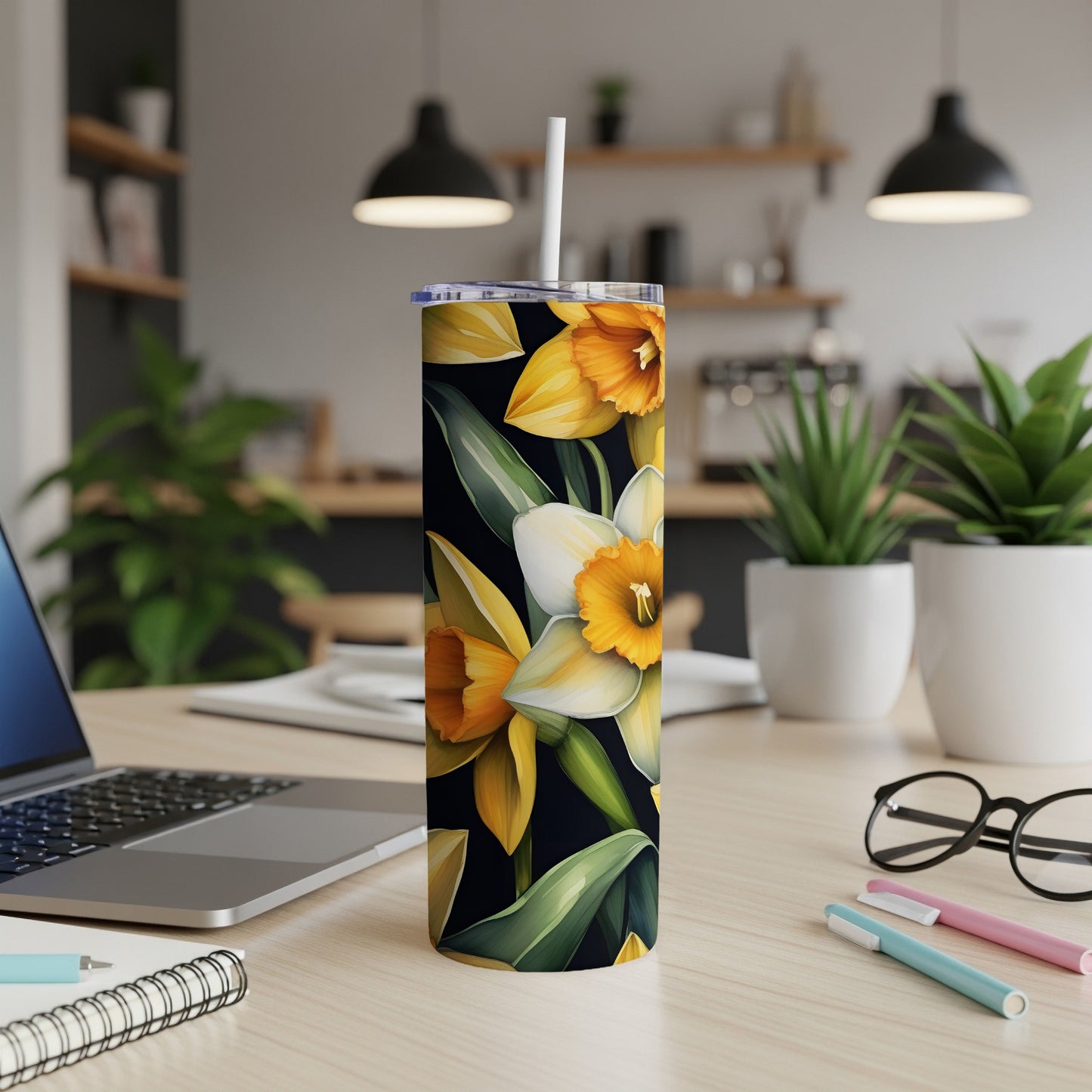 Floral tumbler with daffodils and green leaves on a desk.