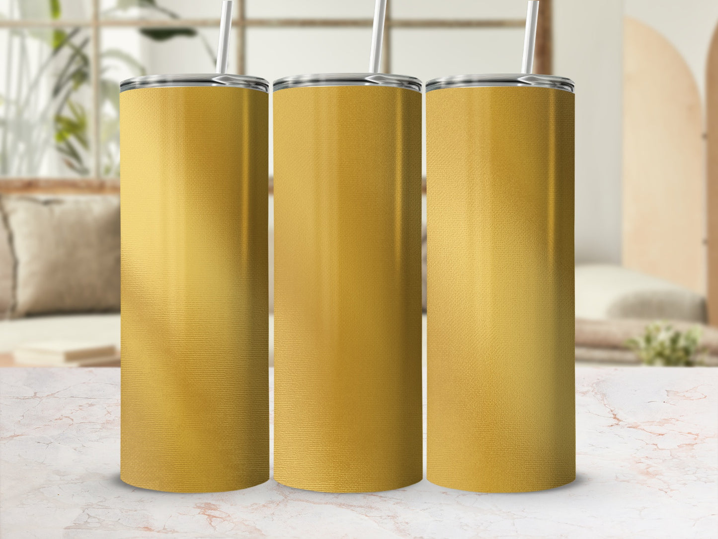 Three gold tumblers with silver lids and straws are displayed on a marble surface.